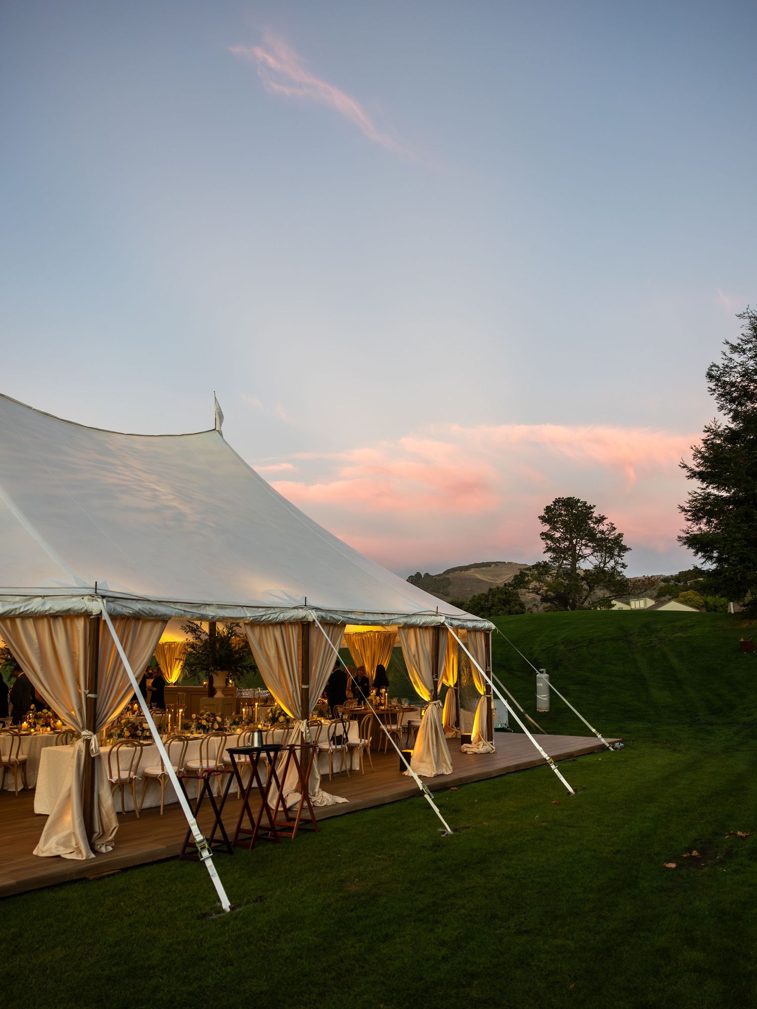 White wedding reception tent glowing with warm light against a dusky sky with soft pink clouds at dusk in California.