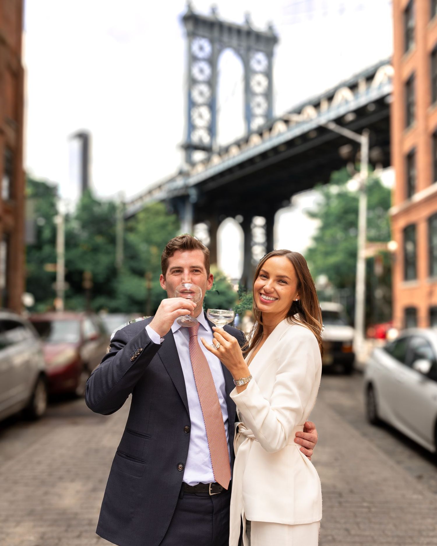Couple toasting with champagne in DUMBO Brooklyn with Manhattan Bridge backdrop on their wedding day.