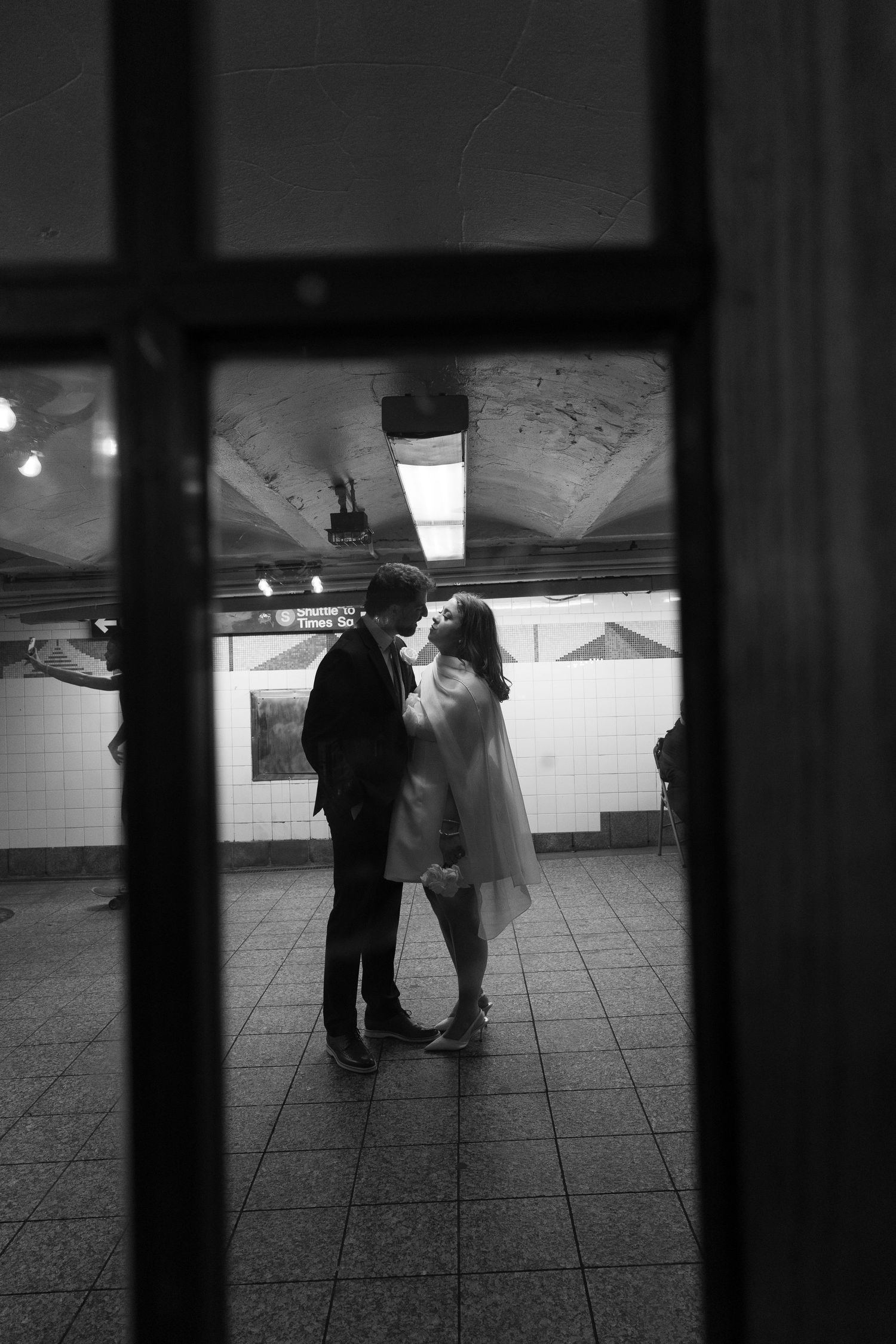 Black and white photo of a couple sharing a romantic moment in a New York City subway station.