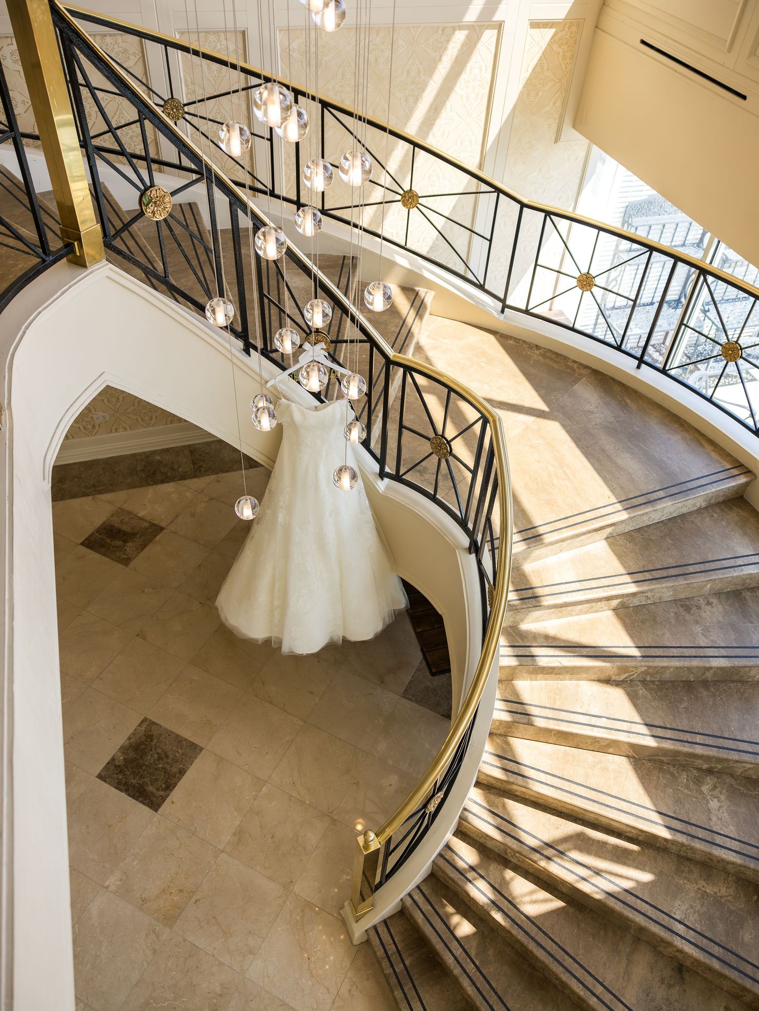 Elegant white wedding gown hanging from grand spiral staircase with crystal chandeliers in the Bronx New York City, in Glen Cove.