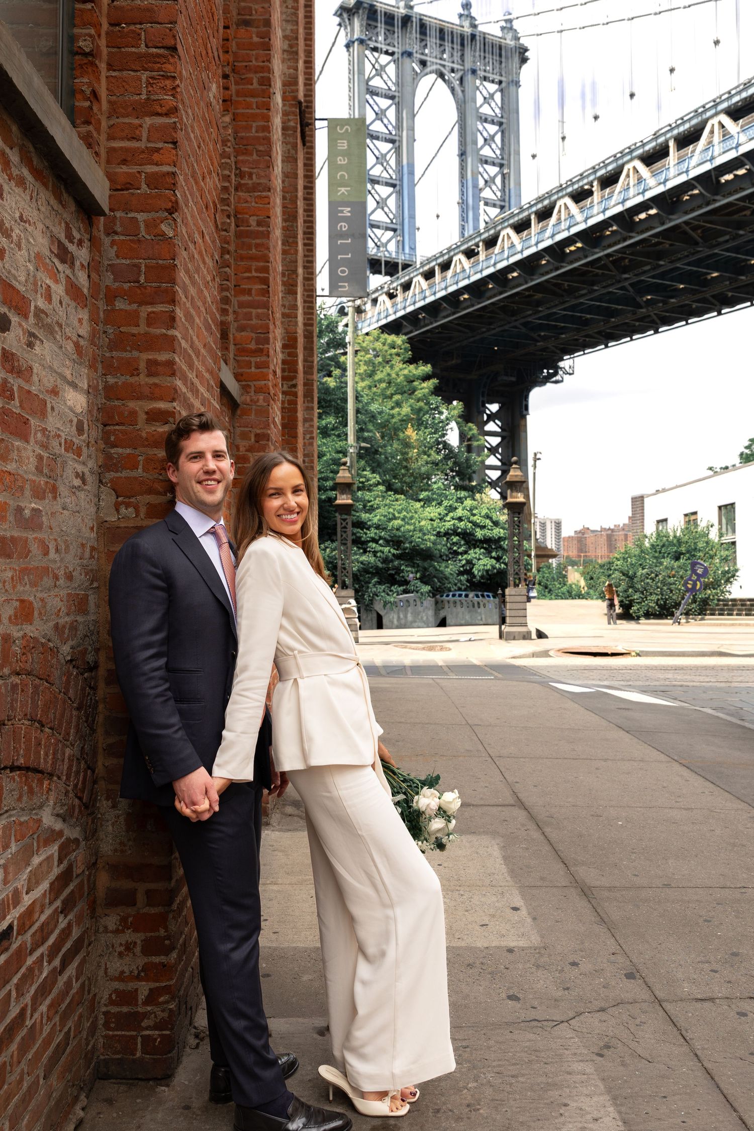 Couple in wedding attire holding hands near Manhattan Bridge in DUMBO, Brooklyn, NYC.