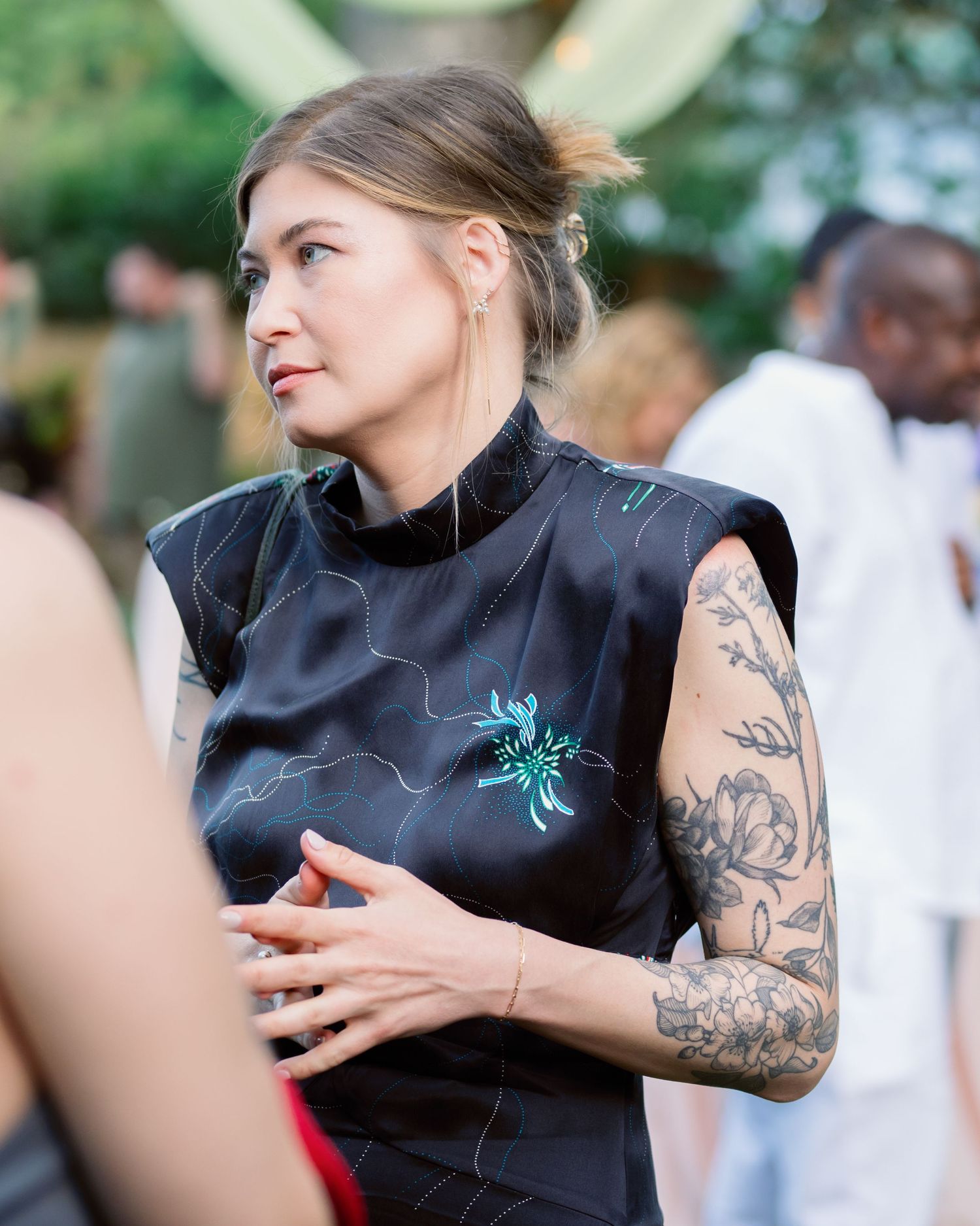 Person in black sleeveless top with visible arm tattoos gestures during animated conversation.