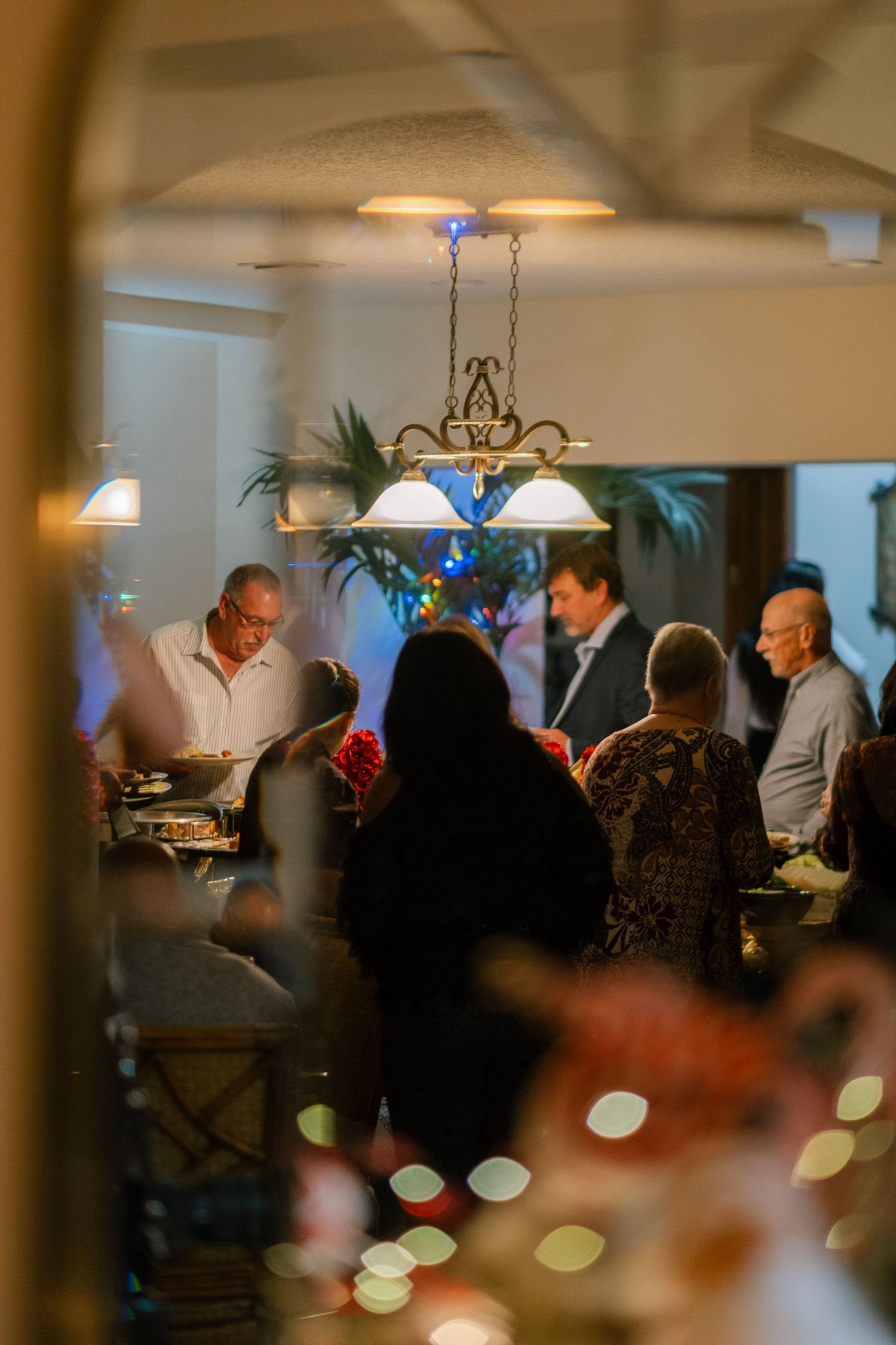 A dimly lit holiday party scene with people mingling and dining under decorative lighting.