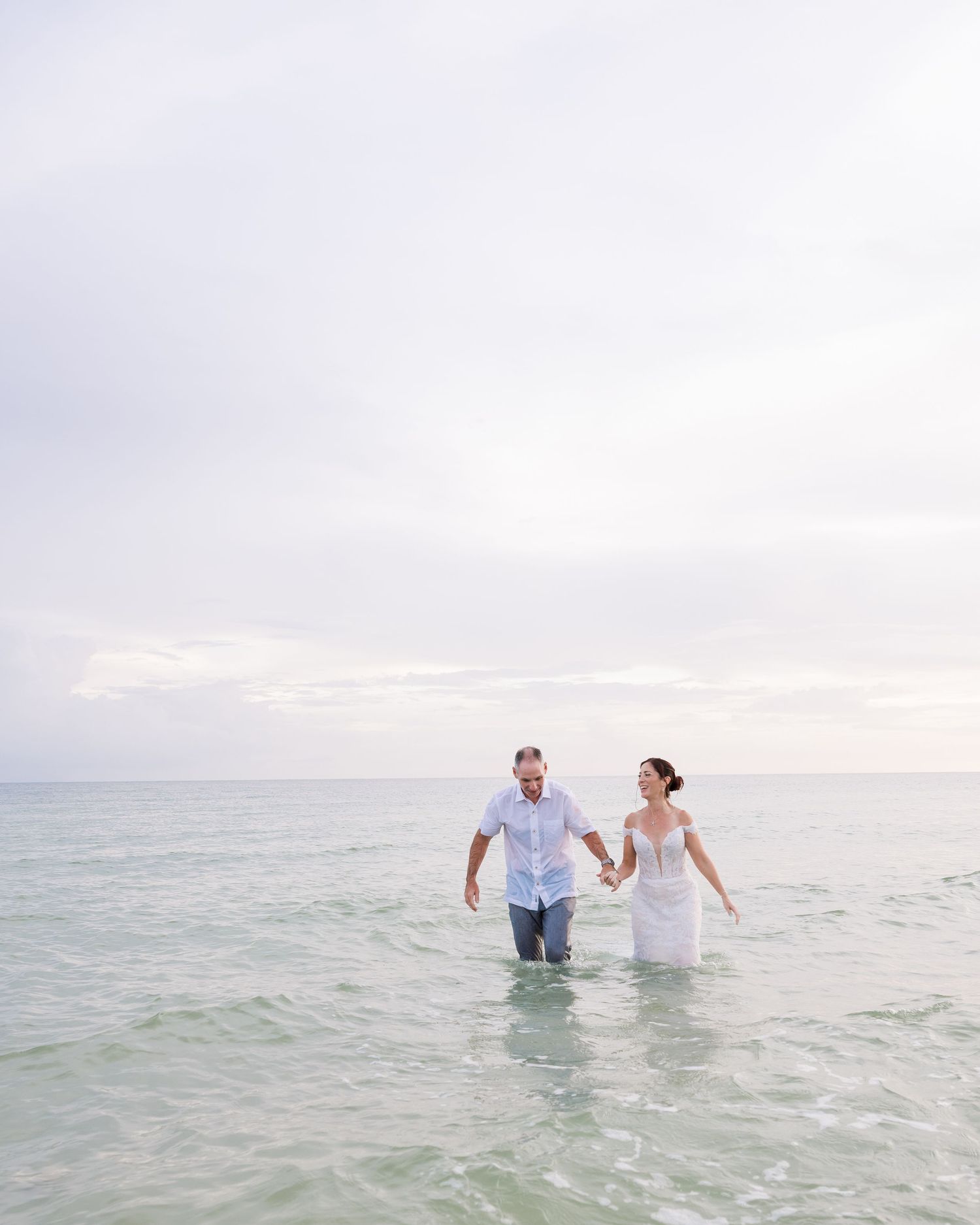 A couple wades together in crystal clear ocean waters during sunset.
