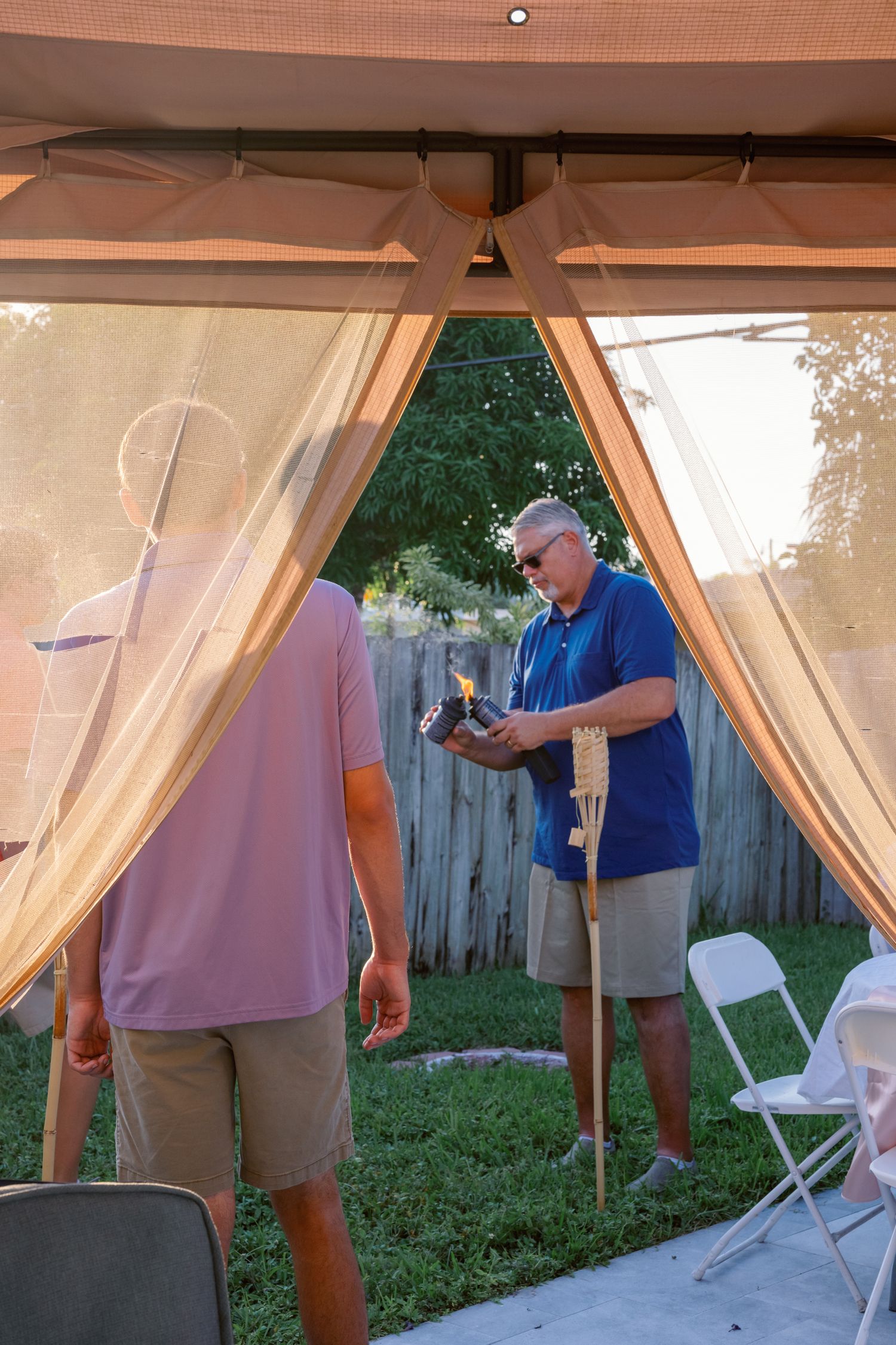 People setting up a backyard party tent with sheer curtains.