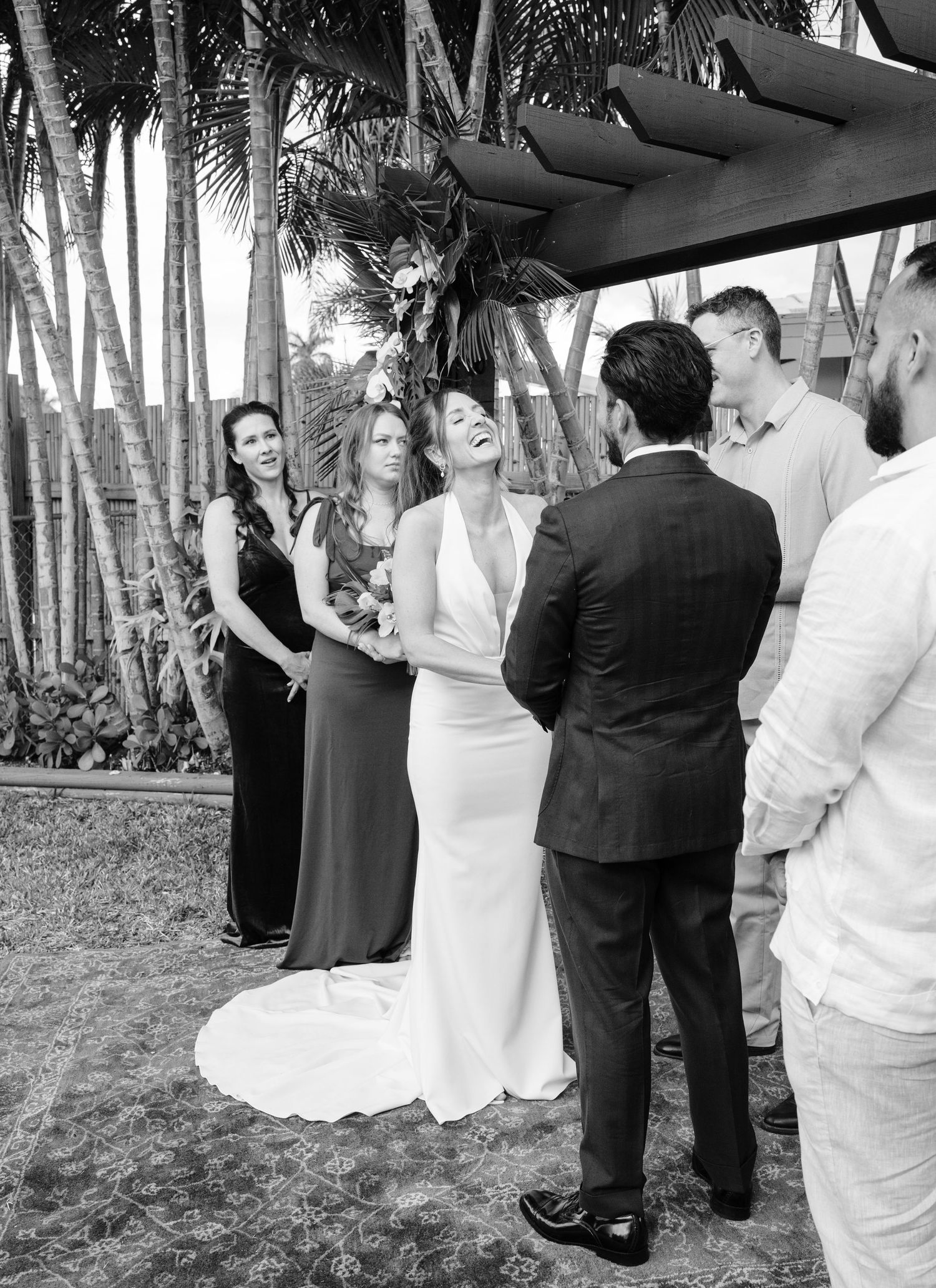 Wedding party dancing outdoors among palm trees in a tropical garden setting.