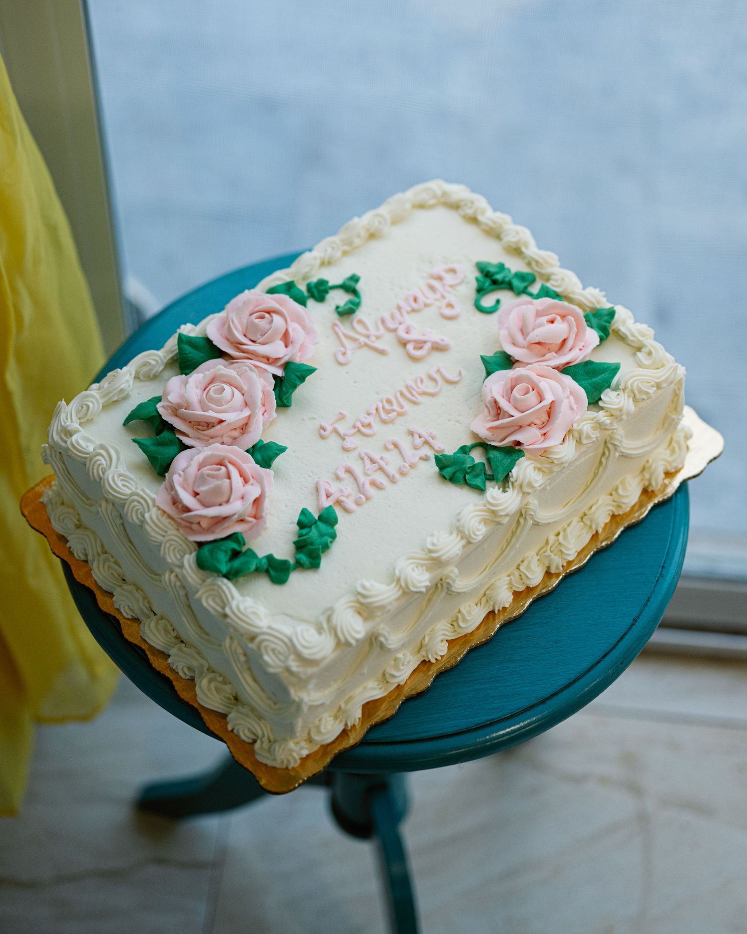 White wedding cake with pink sugar roses and delicate piping displayed on turquoise cake stand.