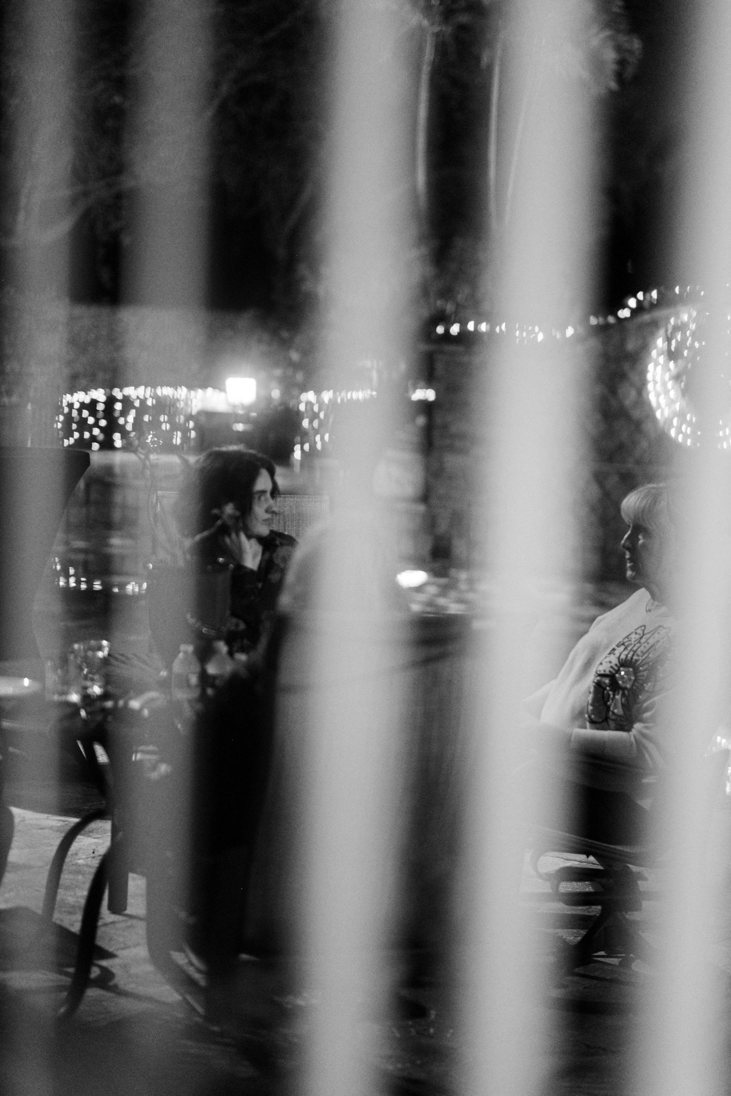 Black and white image of city lights seen through vertical bars creating an abstract pattern of light and shadow.
