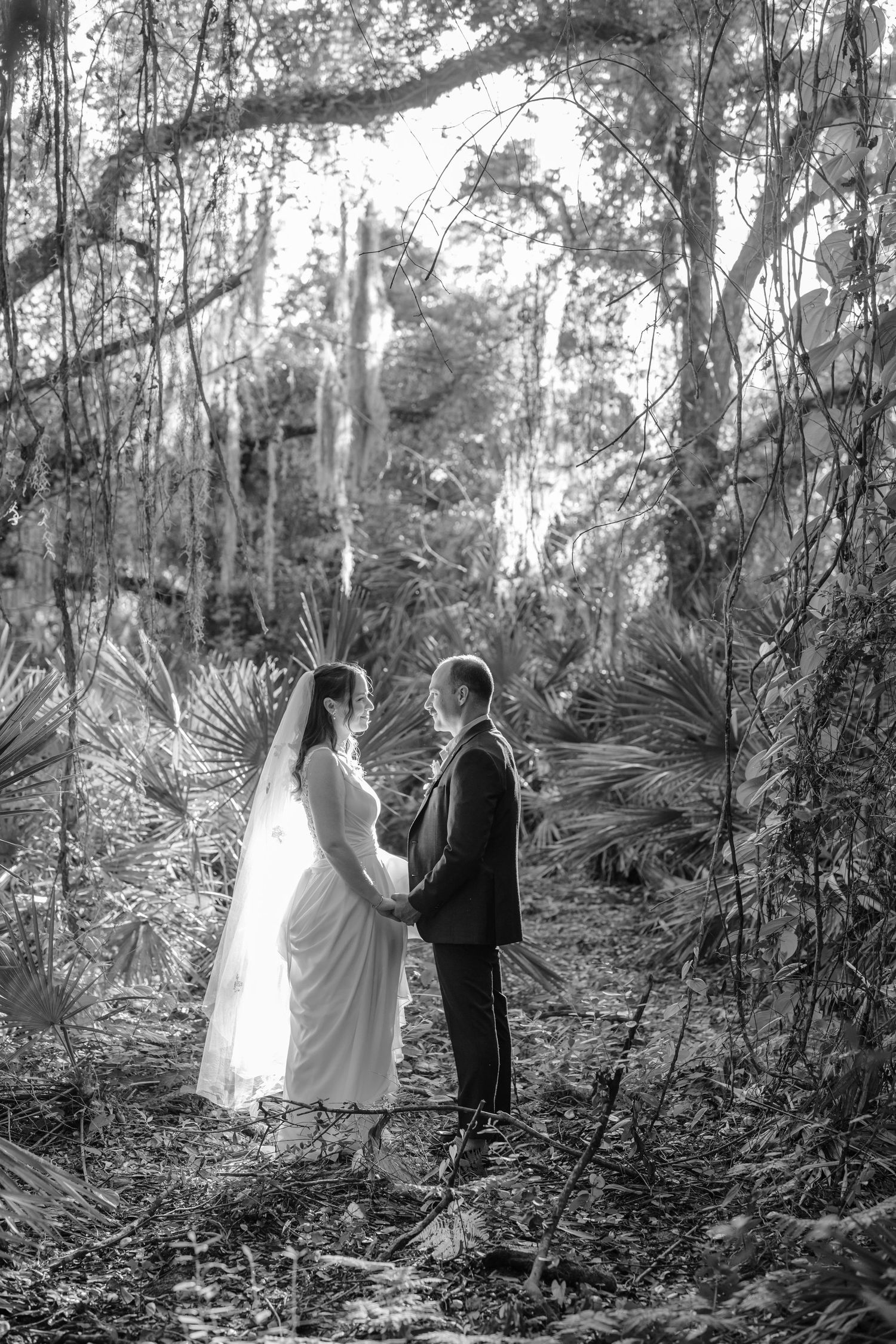 Black and white photo of a couple walking through a wooded path with palm fronds.