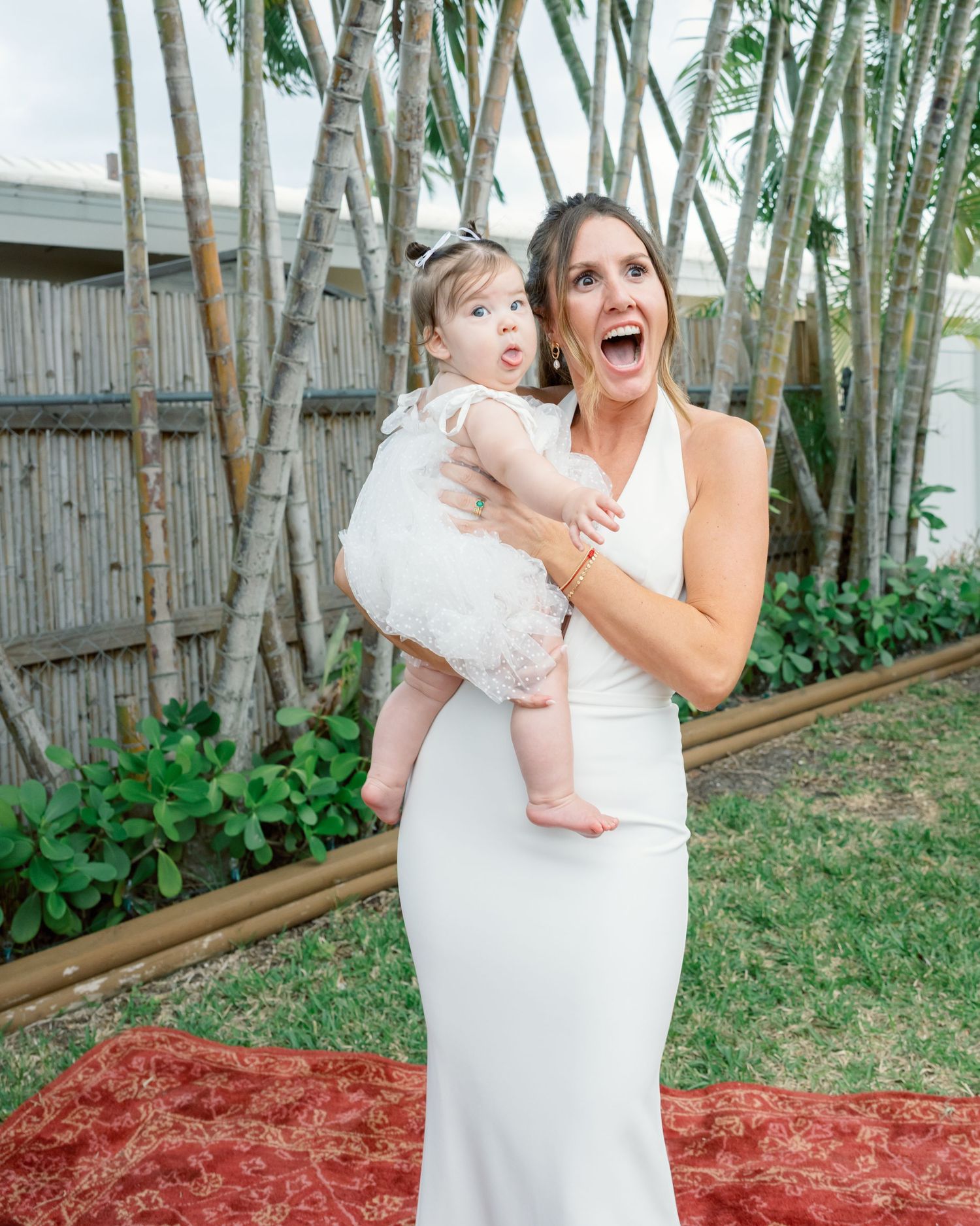 Playful outdoor wedding photos with bamboo backdrop showing mother and child in white dresses.