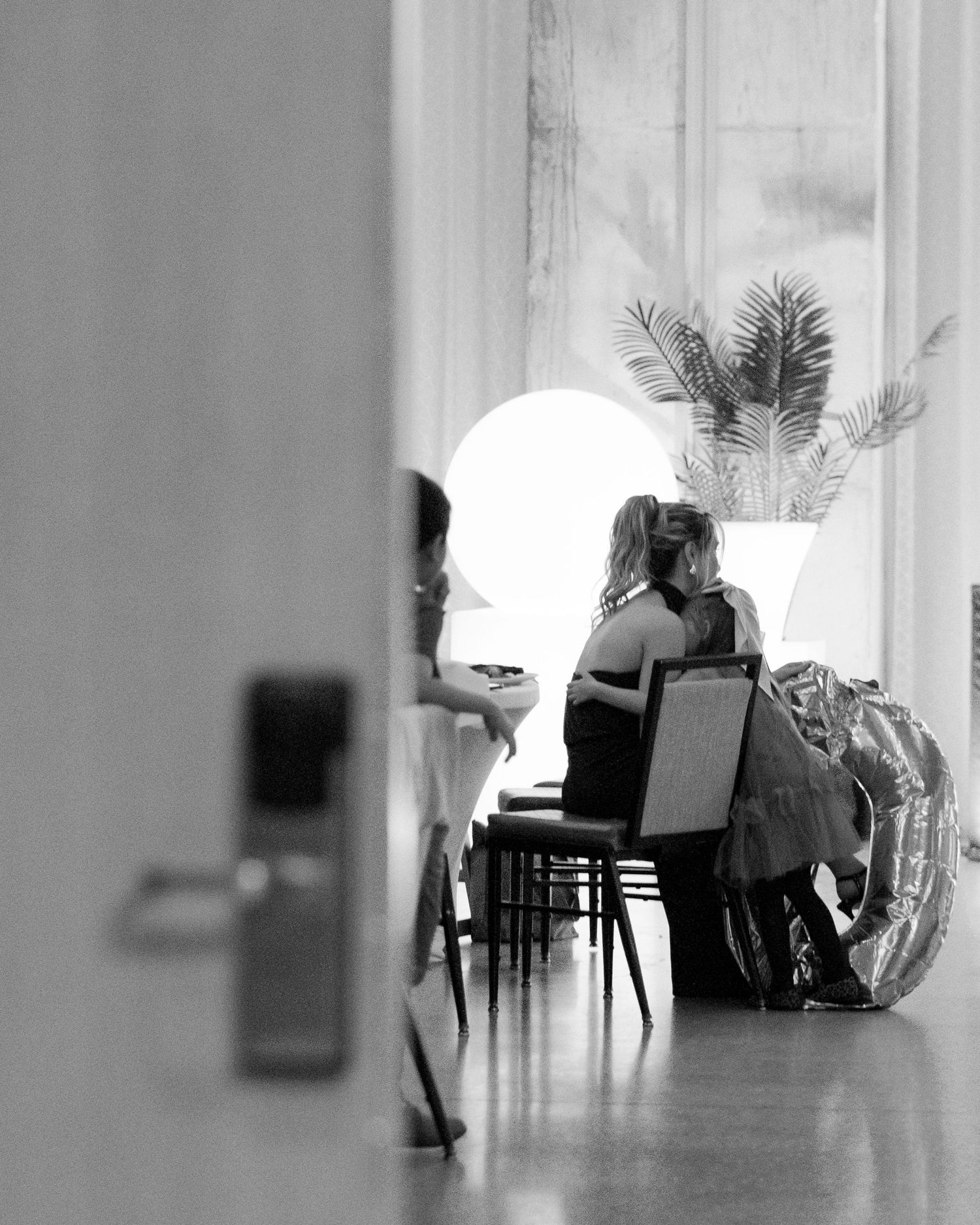 Silhouetted figures in a bright white room with chairs and tables creating a minimalist artistic composition.