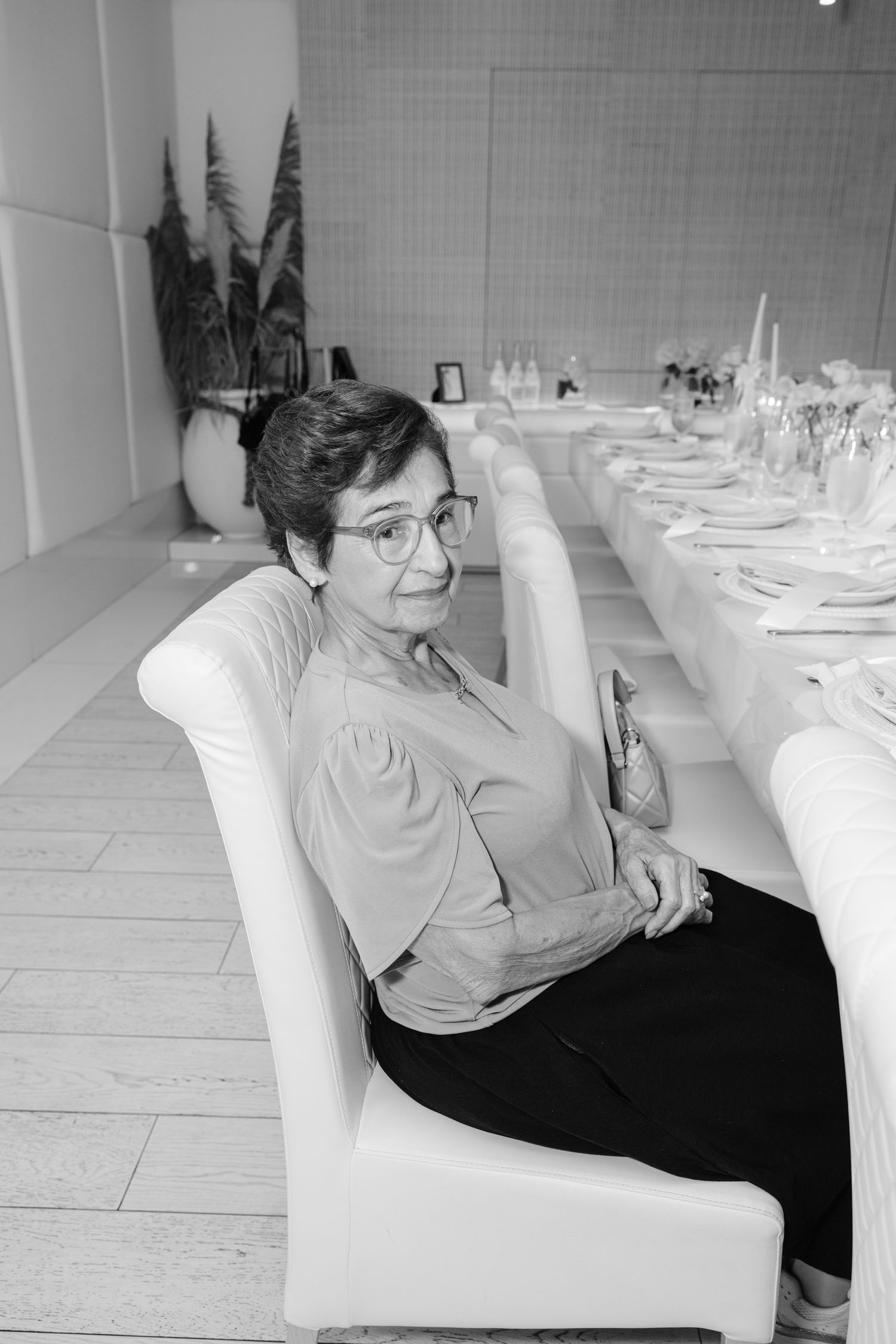 Black and white photo showing someone relaxing in a white upholstered chair in an elegant dining room setting.