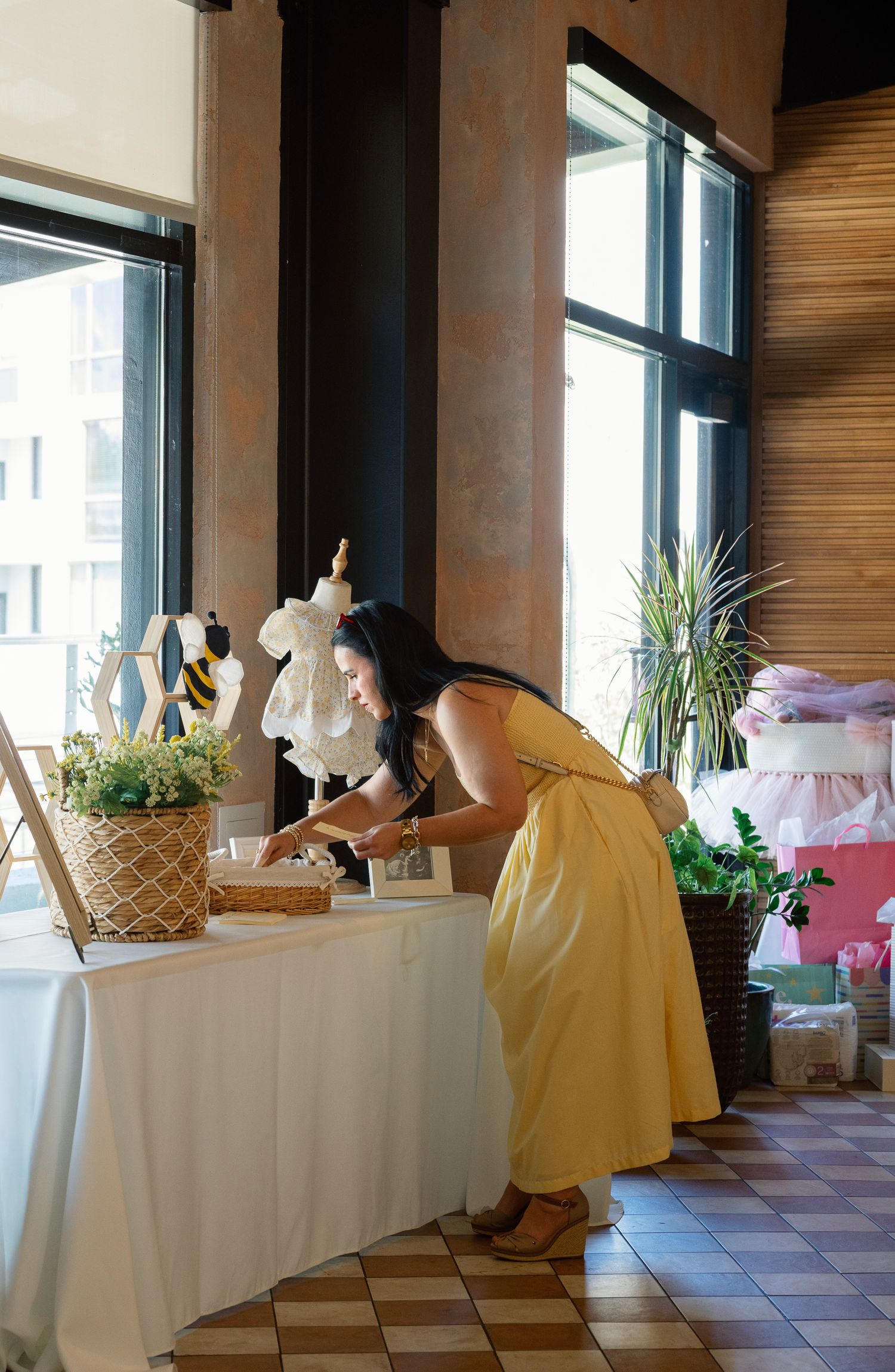 Yellow and white dresses displayed on mannequins with baby shower gifts and decorations on tables by large windows.