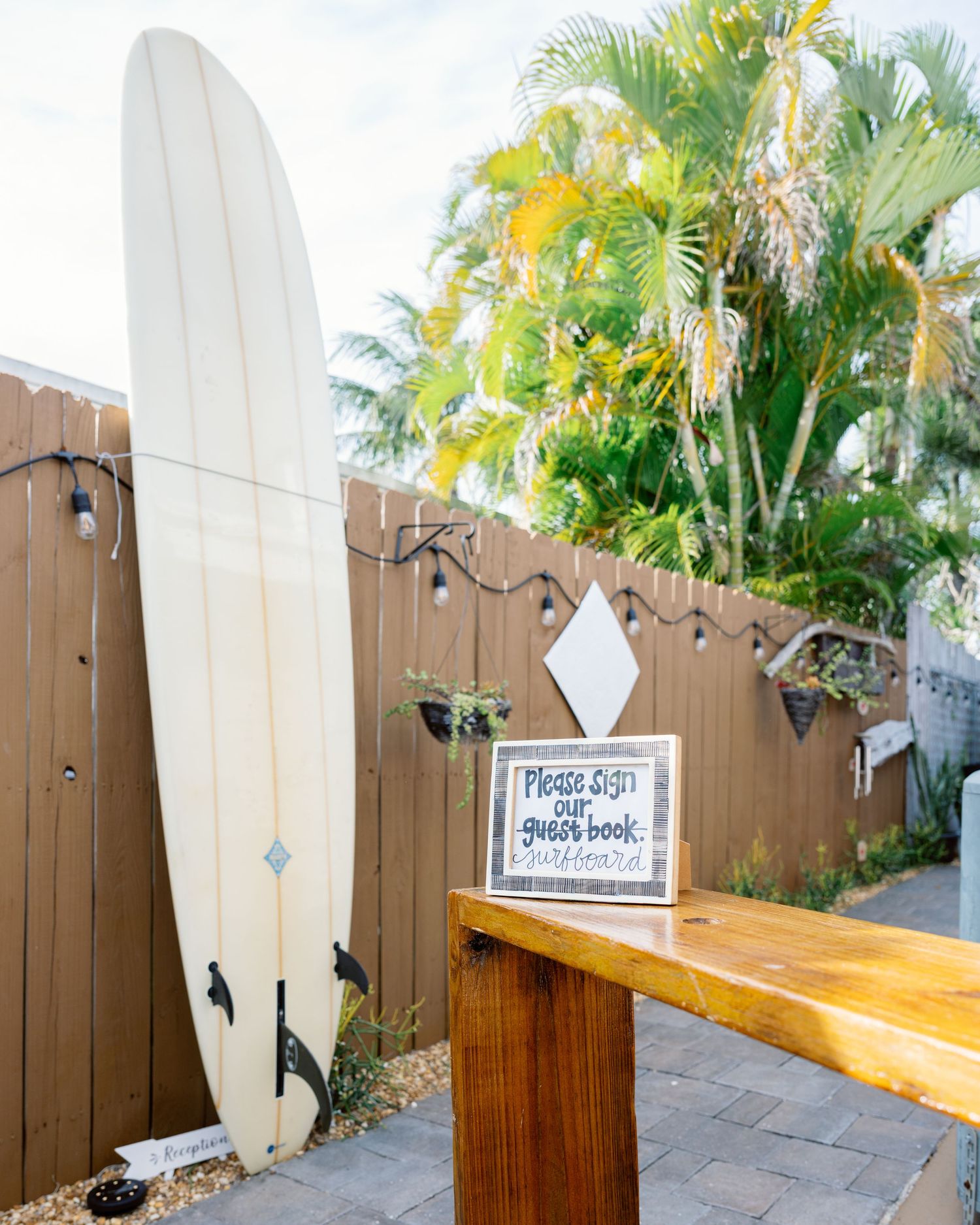 Surfboards line a wooden fence at a beach-themed wedding venue with palm trees in the background.