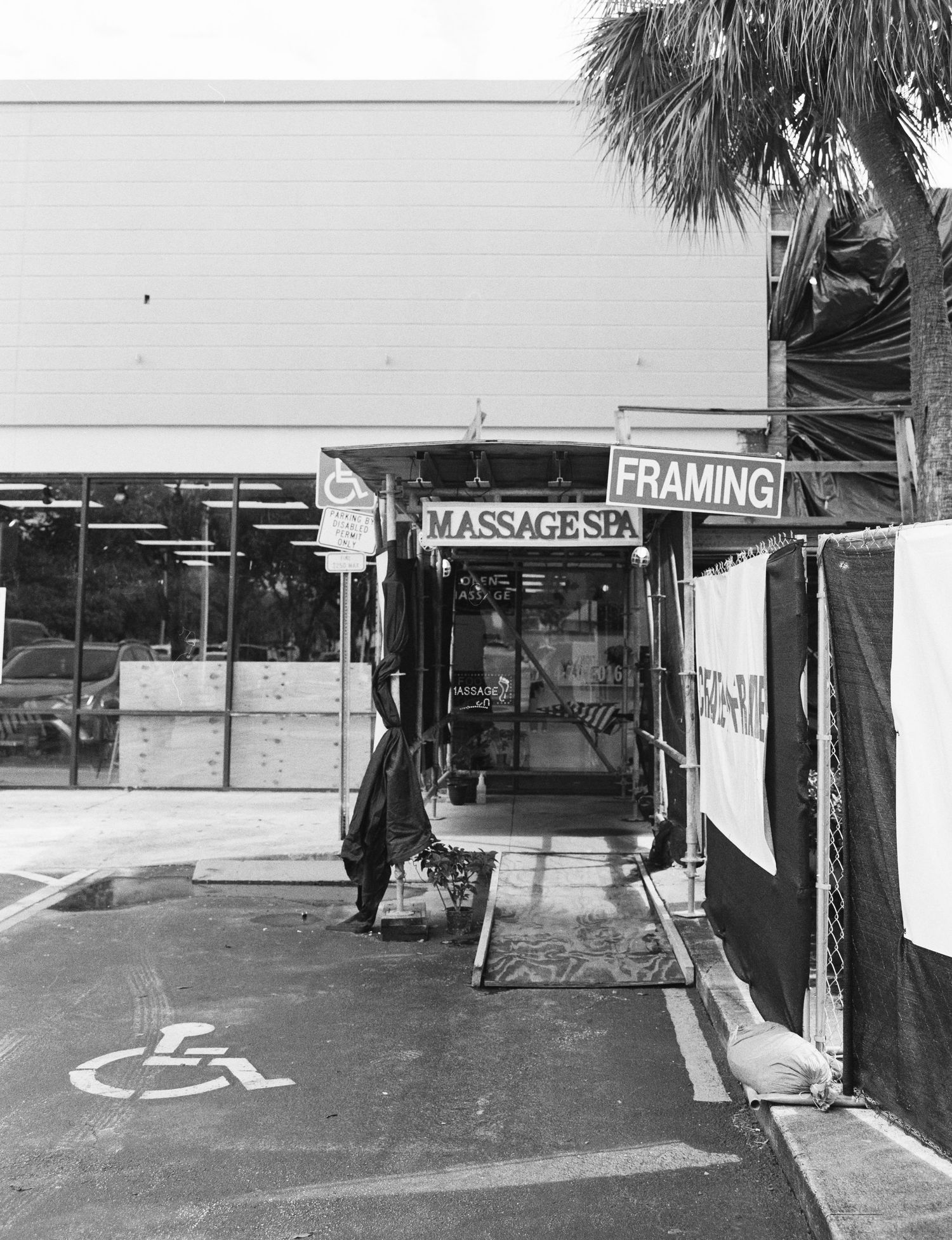 Black and white photo of a strip mall storefront featuring a Massage Spa and Framing shop with handicap parking.