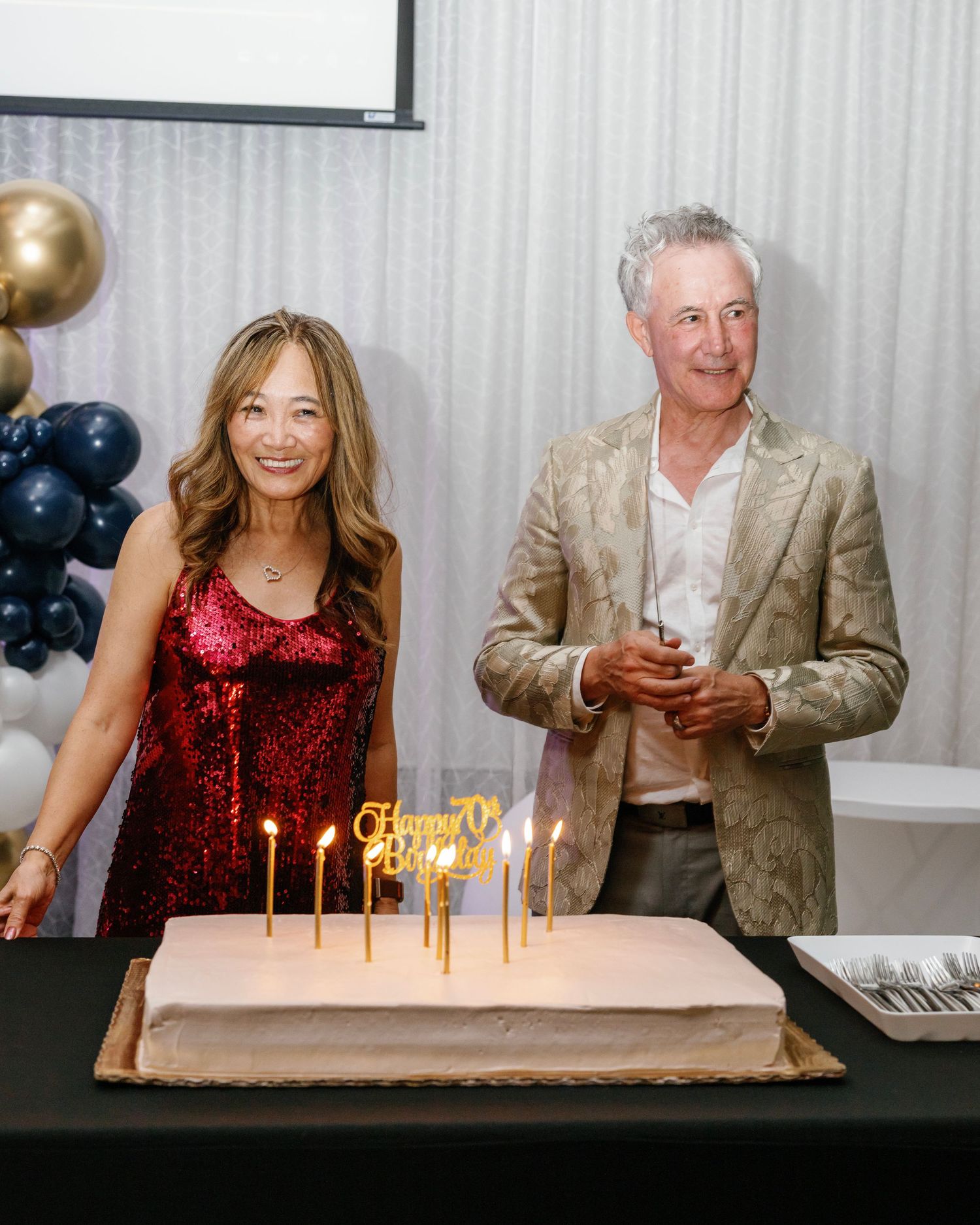 Birthday celebration scene with lit candles on a table and people in formal attire.