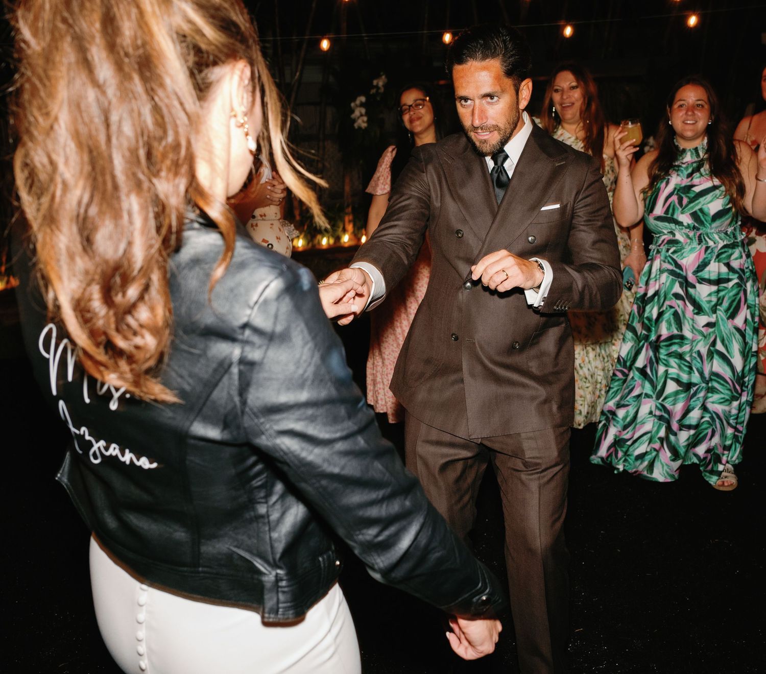 People dancing in formal attire at an evening event with string lights overhead.
