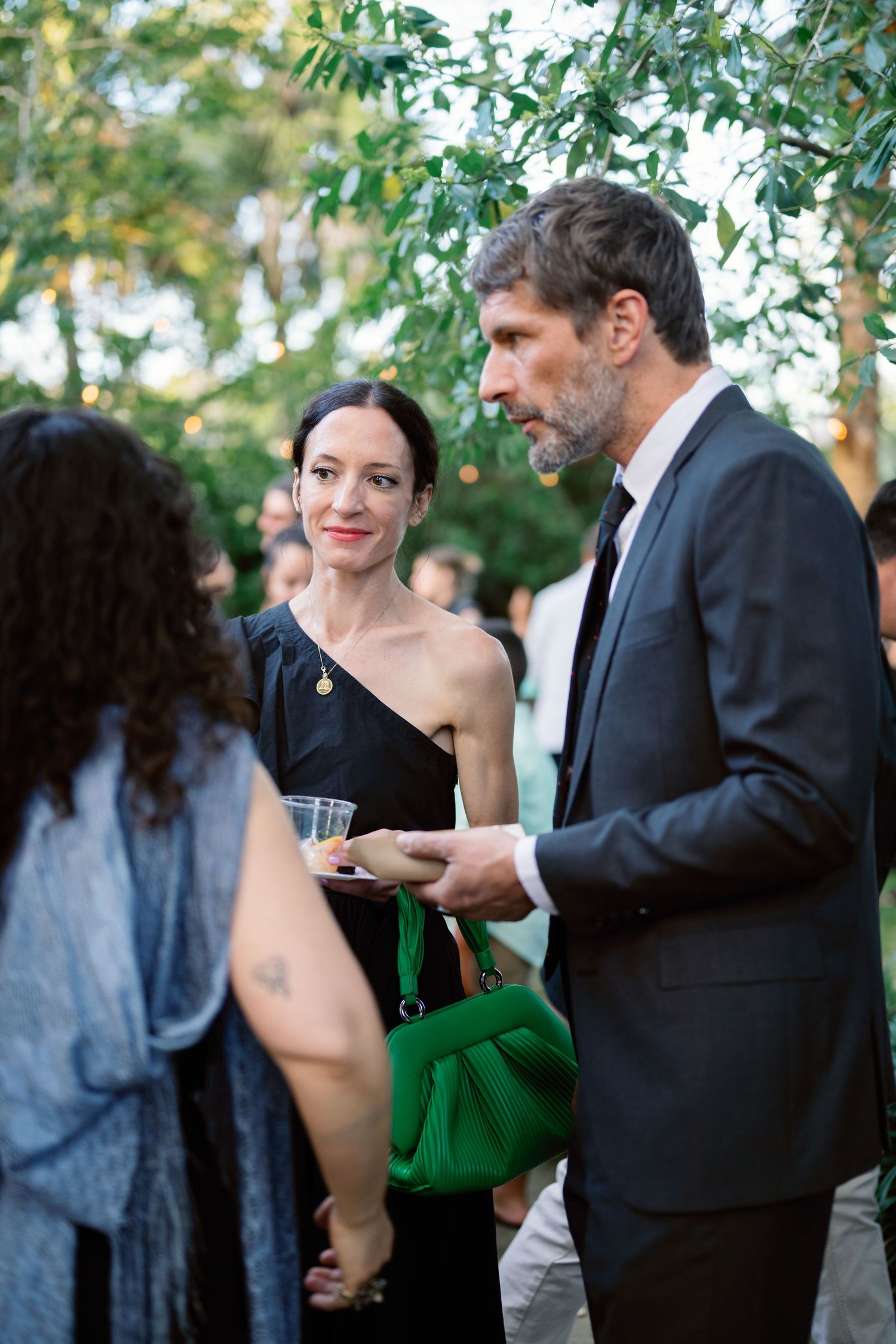Guests mingling at an elegant outdoor event with lush greenery in the background.