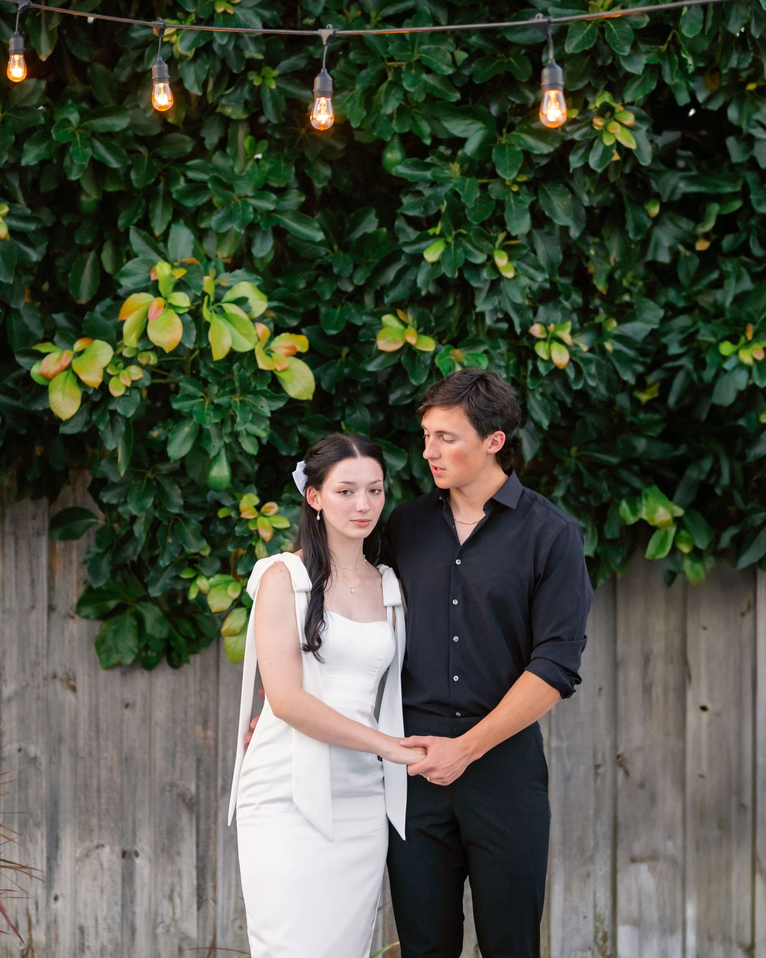 String lights illuminate garden setting with wooden fence and lush green foliage backdrop.