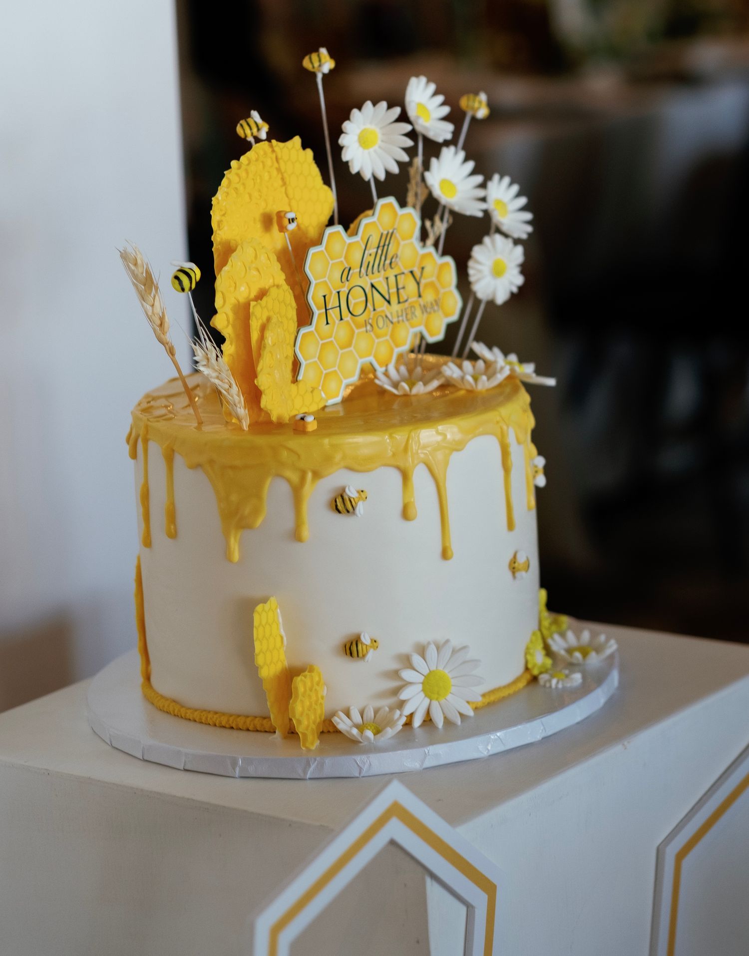 White wedding cake with yellow honey drip decoration and daisy flowers on top.
