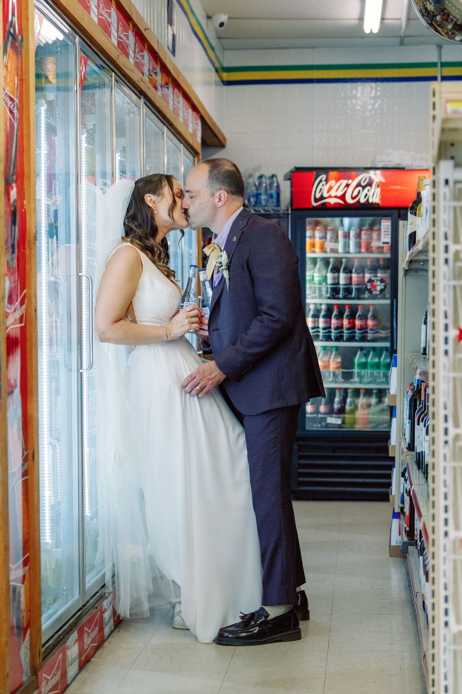 A couple shares a moment in a convenience store aisle with Coca-Cola refrigerators.