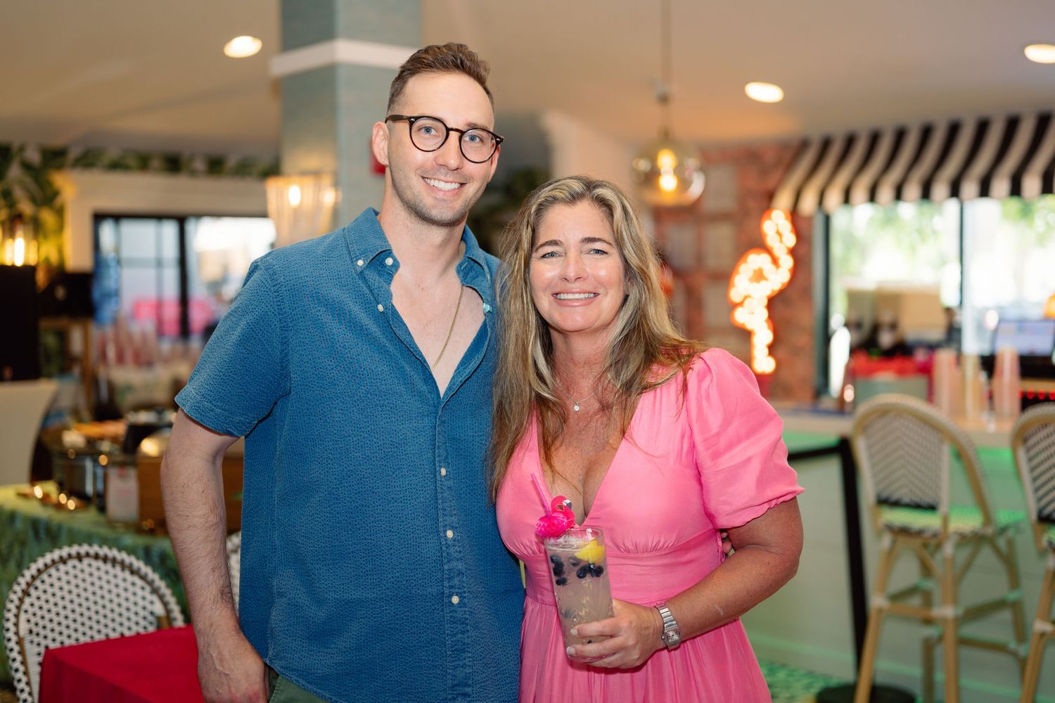 Couple enjoying drinks and smiling at a tropical-themed bar with warm lighting.