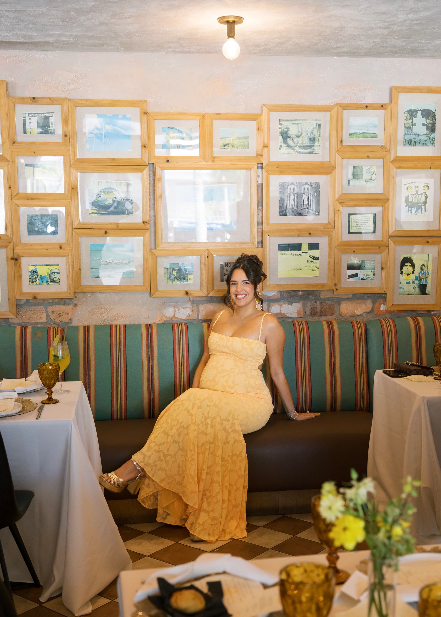 A yellow dress adorned guest sits in a restaurant booth decorated with framed artwork on the wall.