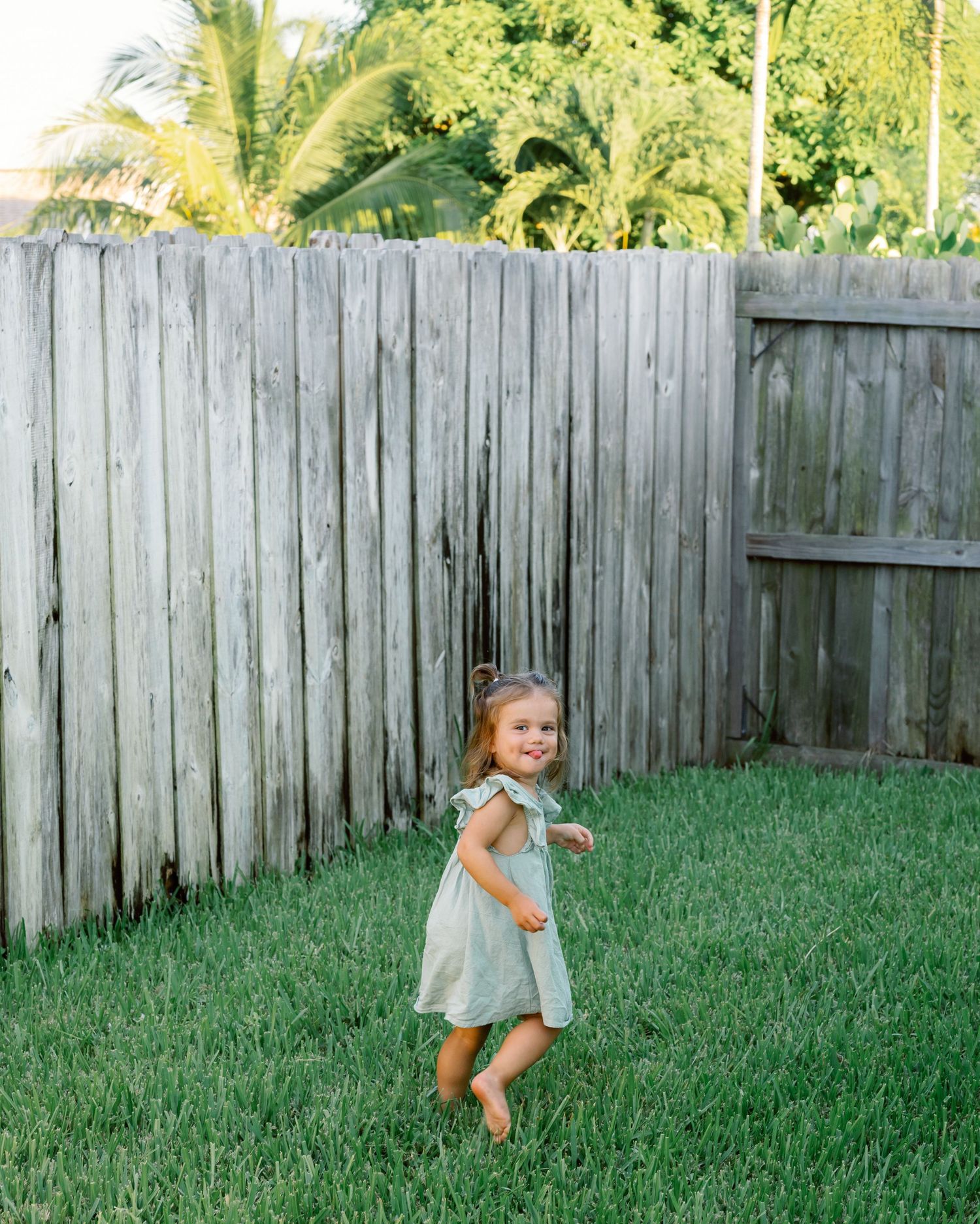 A sequence of photos showing a small child playing and running joyfully on green grass near a wooden fence.