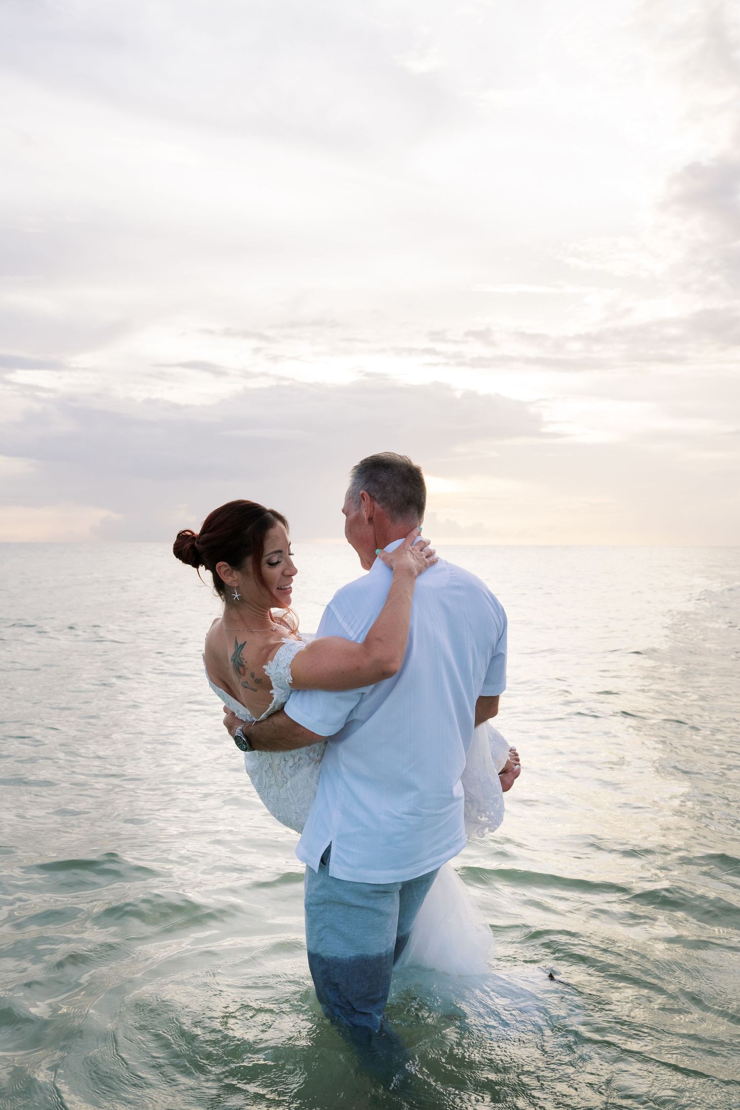 Romantic couple embraces while standing in ocean waters during sunset.