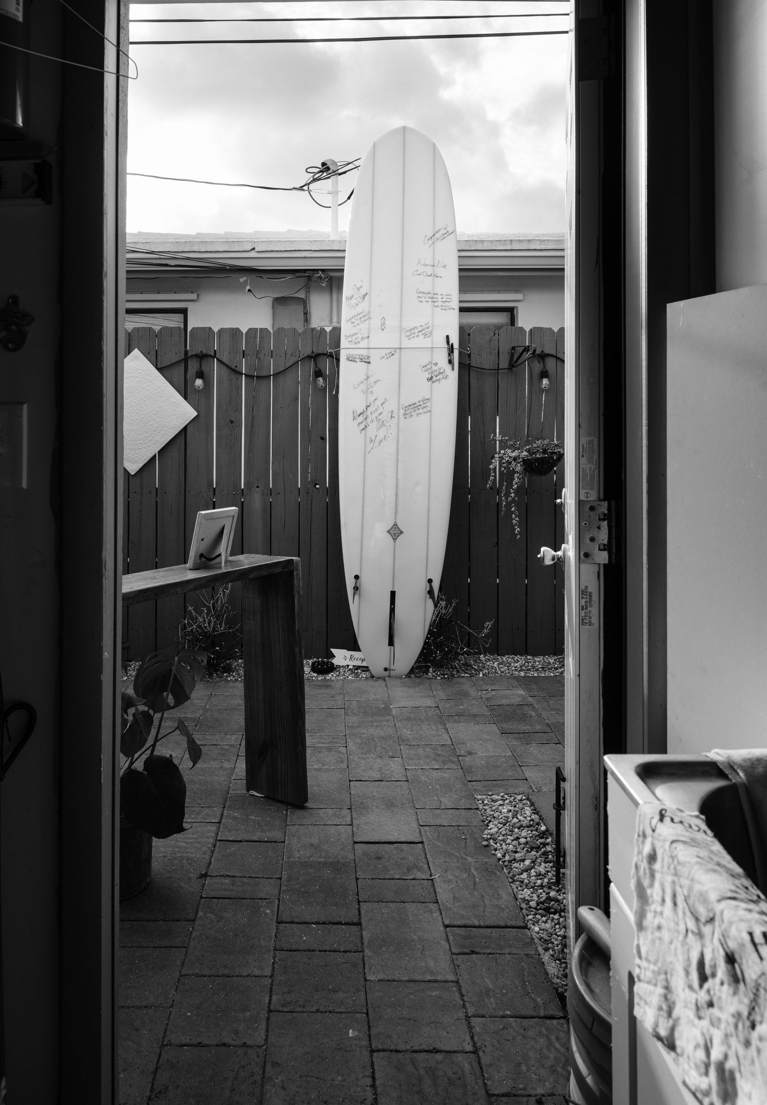 Black and white view of surfboards leaning against fence in outdoor patio area.