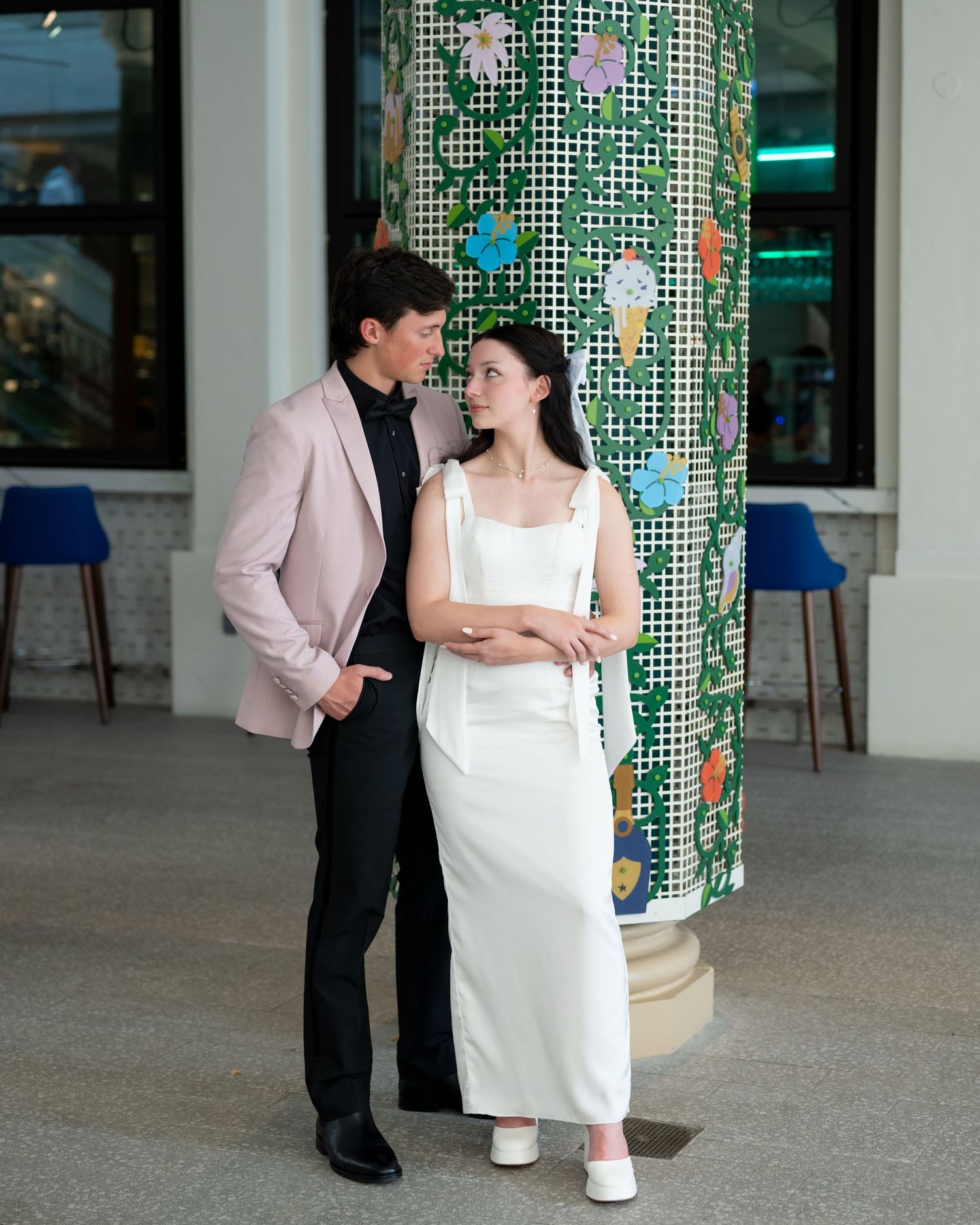 A couple poses romantically by a decorative pillar with floral designs in an indoor setting.