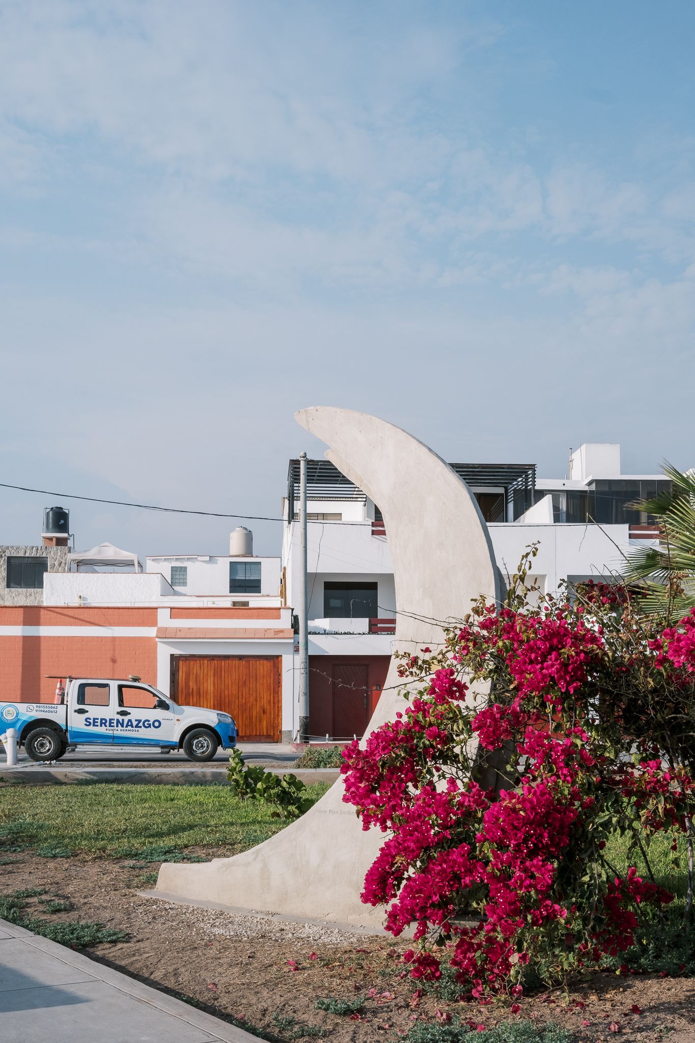 Modern white architecture with bright pink bougainvillea flowers against blue sky.