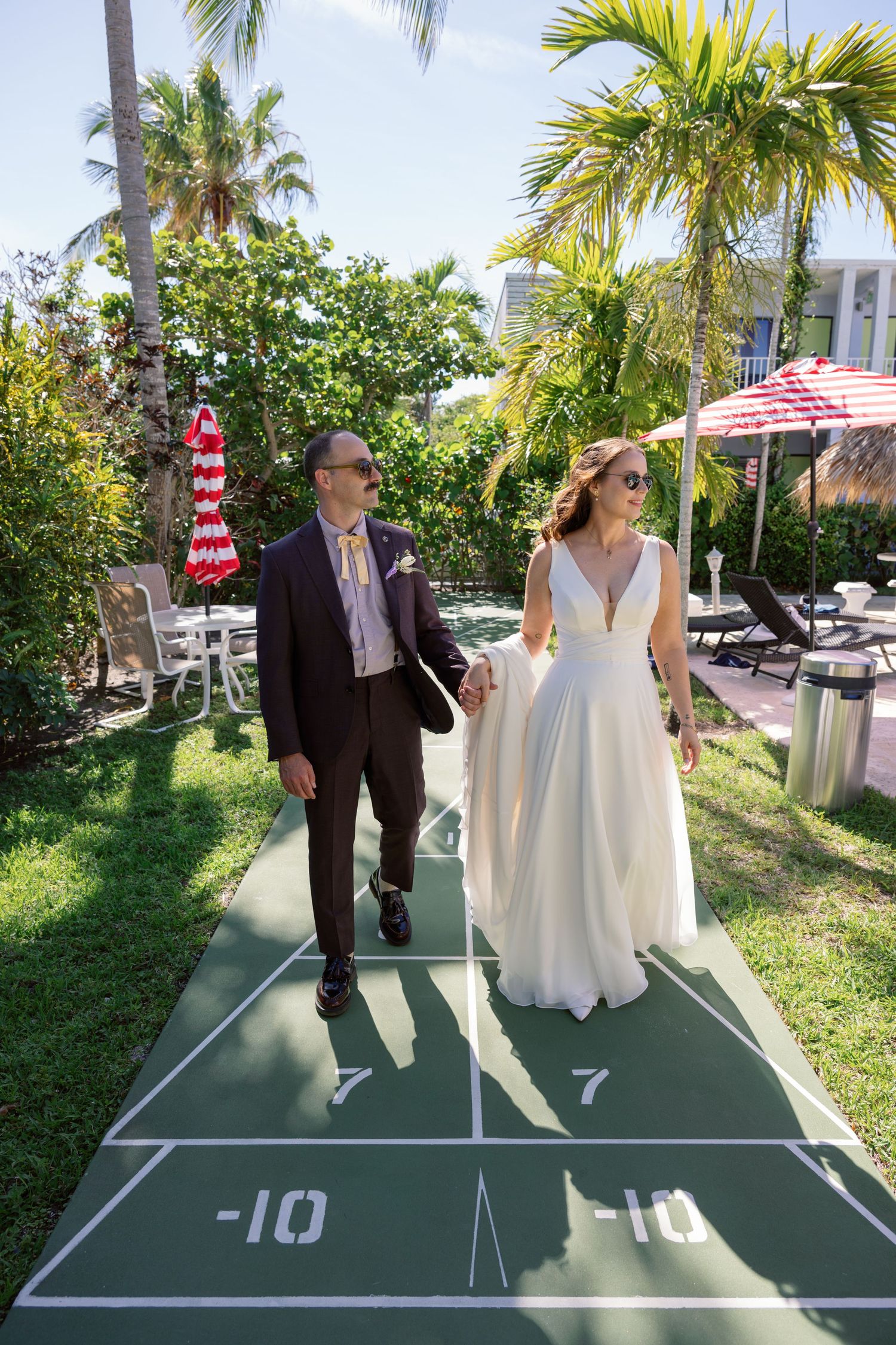 A couple walks along a numbered shuffleboard court with palm trees in the background.