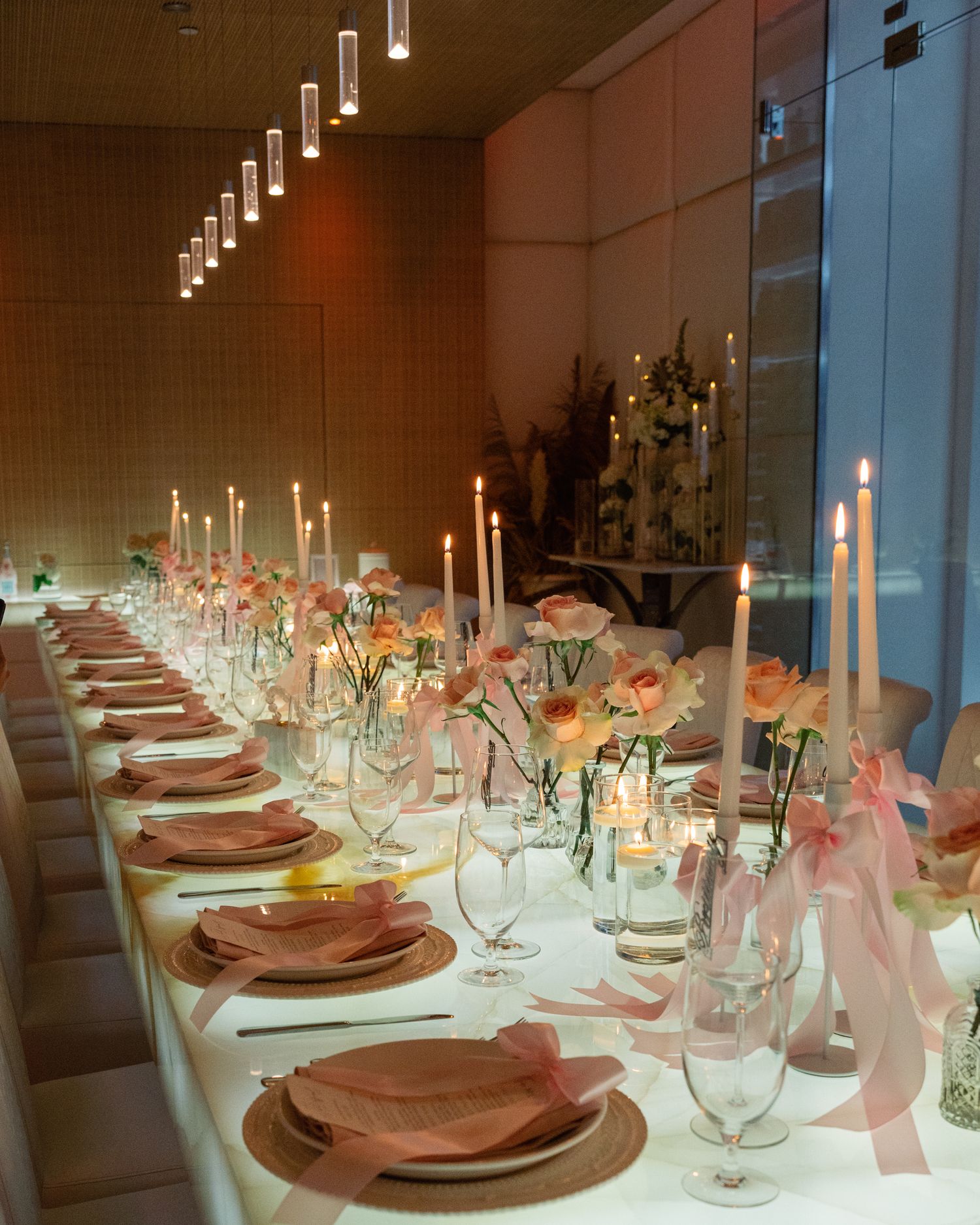Elegant table settings with tall candles, pink accents, and place settings arranged for a formal dinner event.