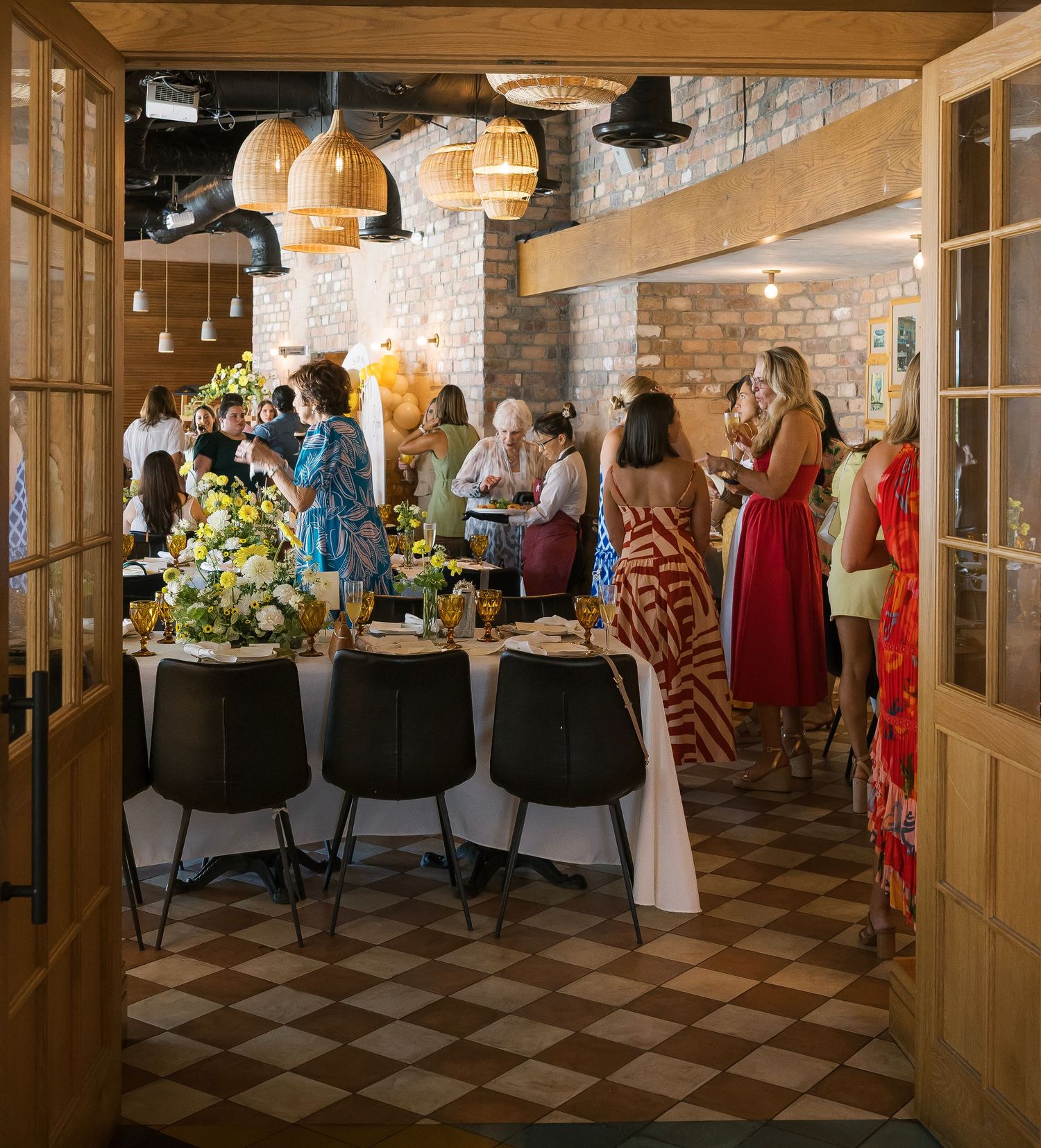 Spacious event venue with exposed brick walls, wooden beams, and checkered floor pattern.