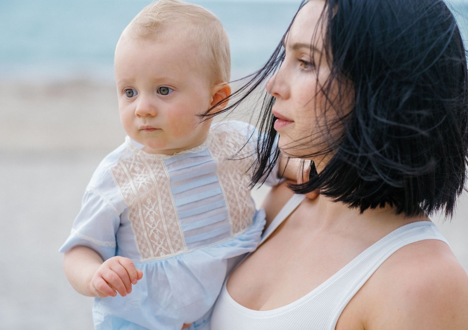 A parent and baby share tender moments together while sitting outdoors in natural light.