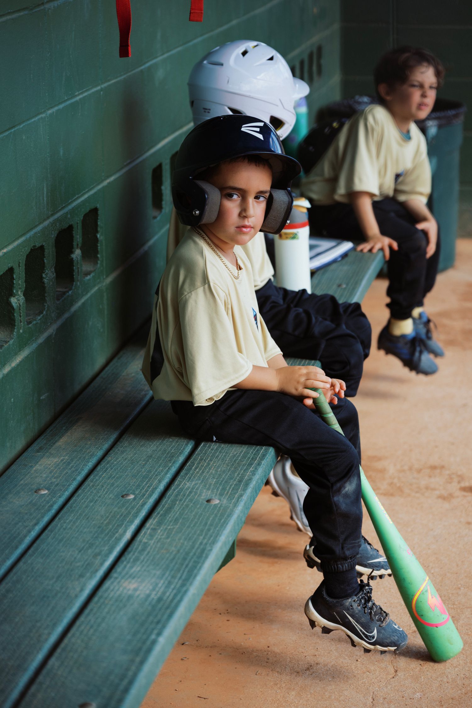 Youth baseball players sitting in dugout with equipment during game.