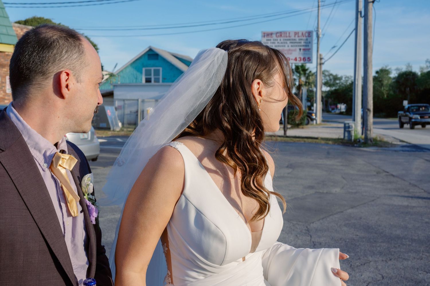 Bride in white gown veil walks with groom outdoors near colorful buildings on their wedding day. Fine Art Photography by Alexandra Dillow