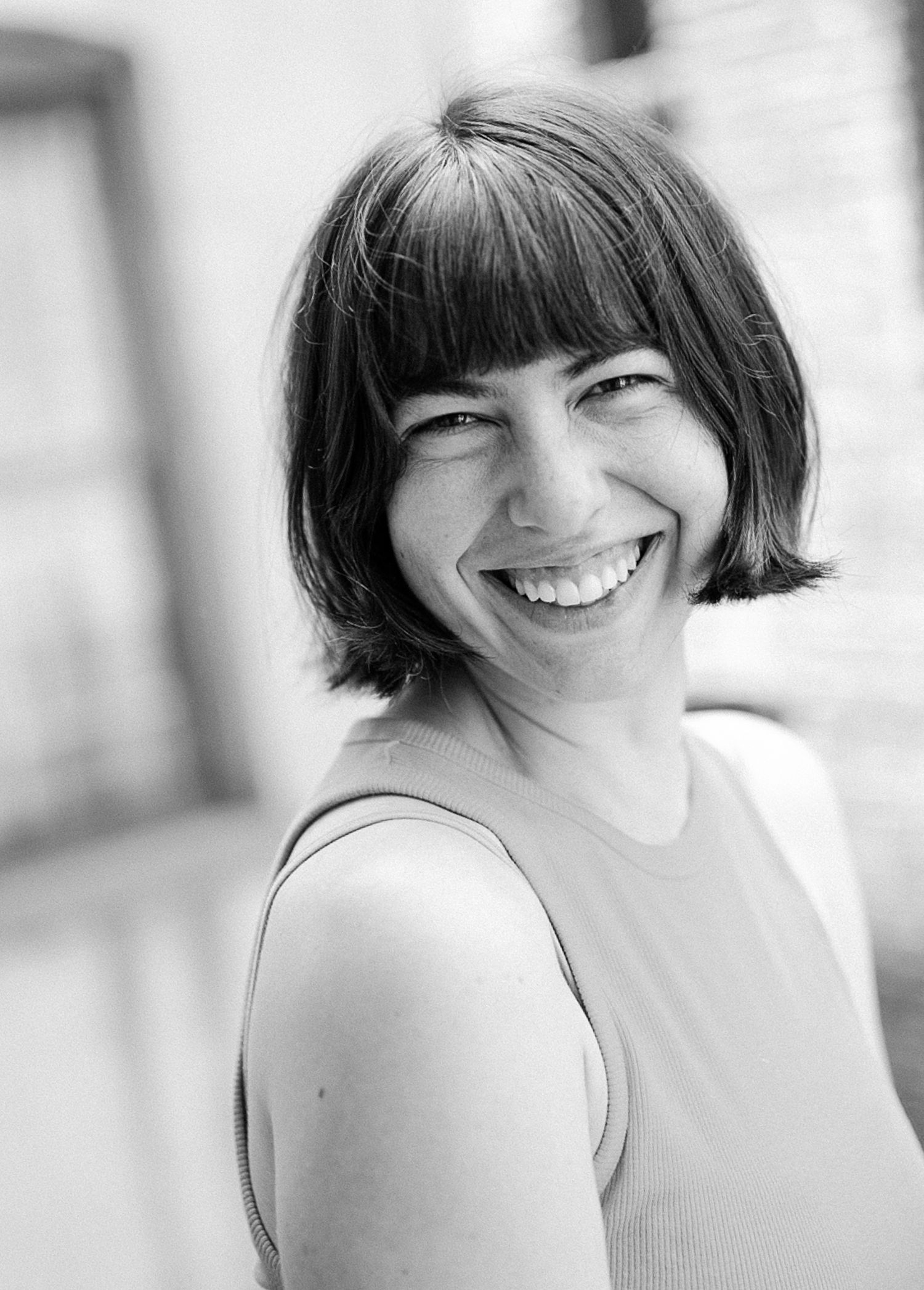 Black and white portrait photograph of a person with short dark hair and bangs smiling warmly at the camera.