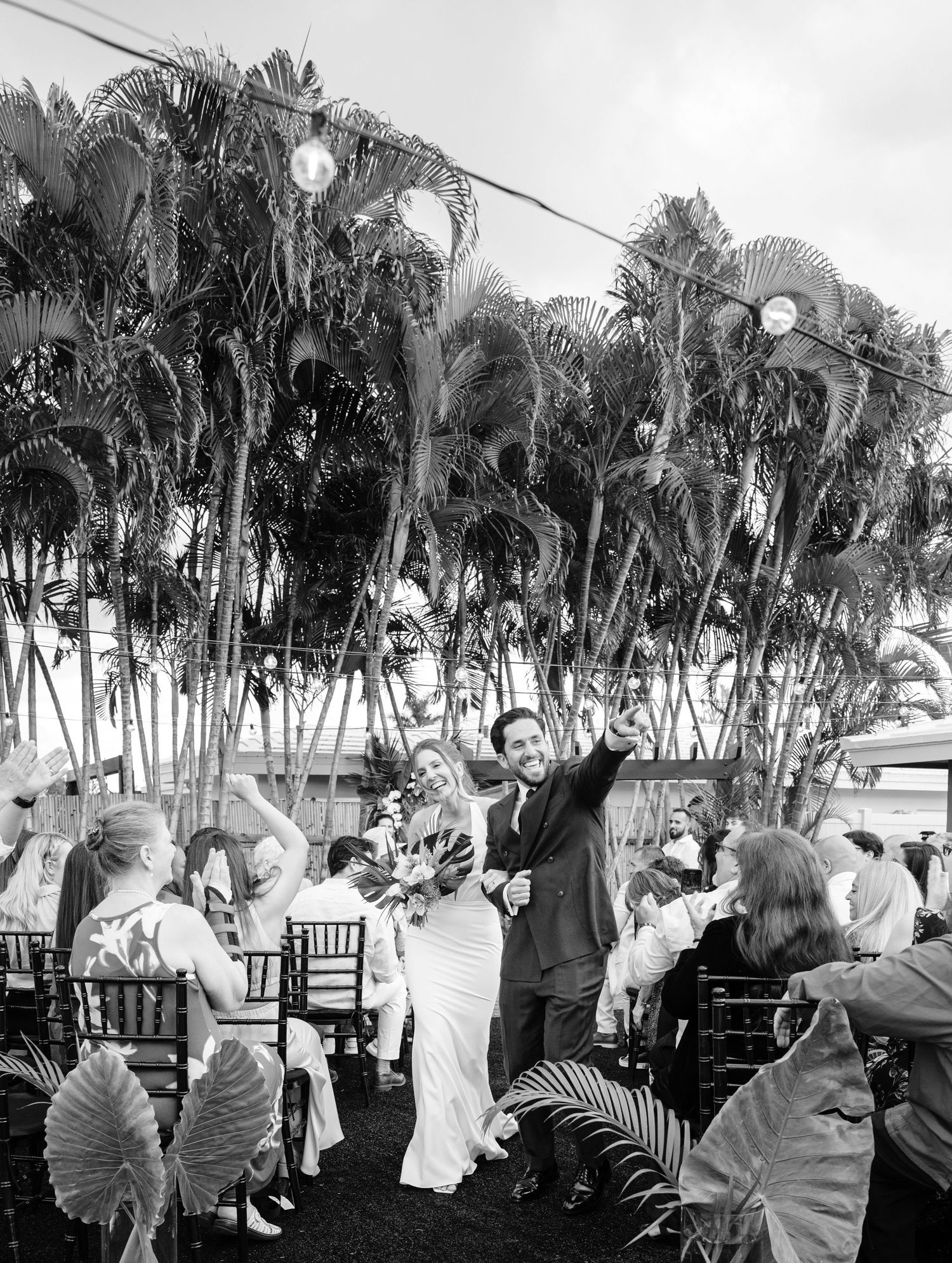 Wedding guests enjoying an outdoor celebration with palm trees in the background during a black and white reception.