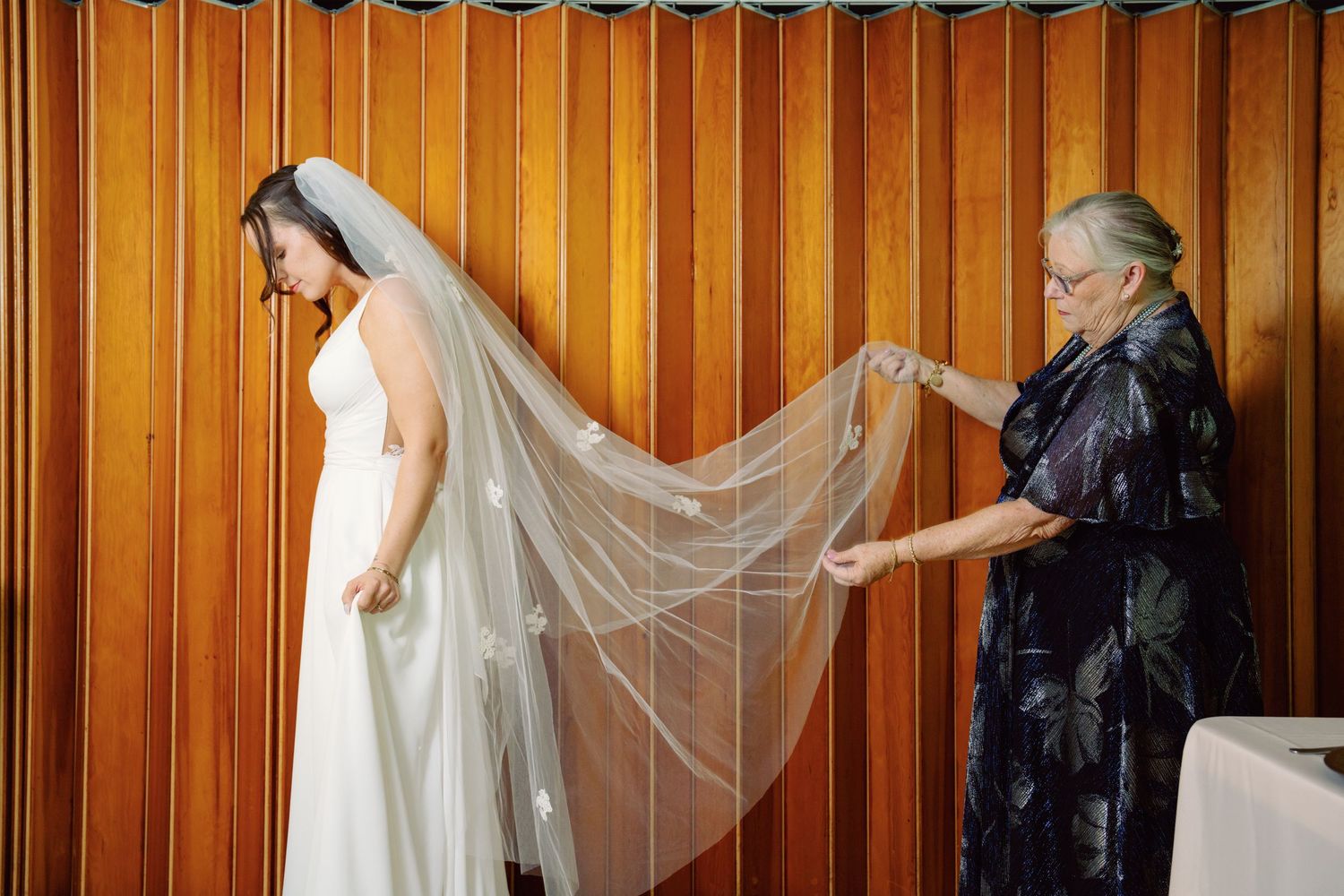 Wedding party poses in front of wood paneled wall with flowing white veils creating elegant lines.