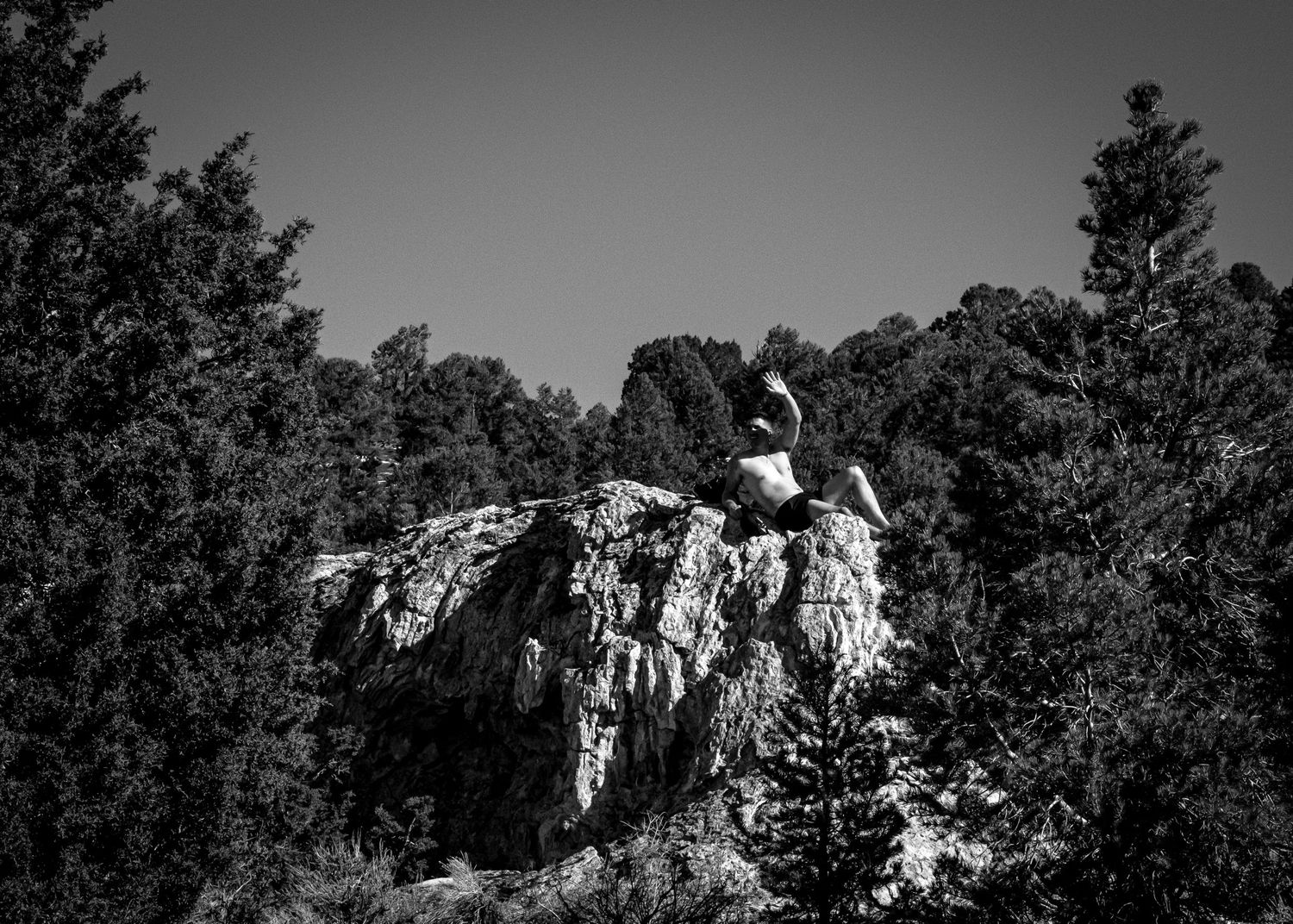 Black and white panoramic view of rocky mountain peaks and cliffs surrounded by dense forest.