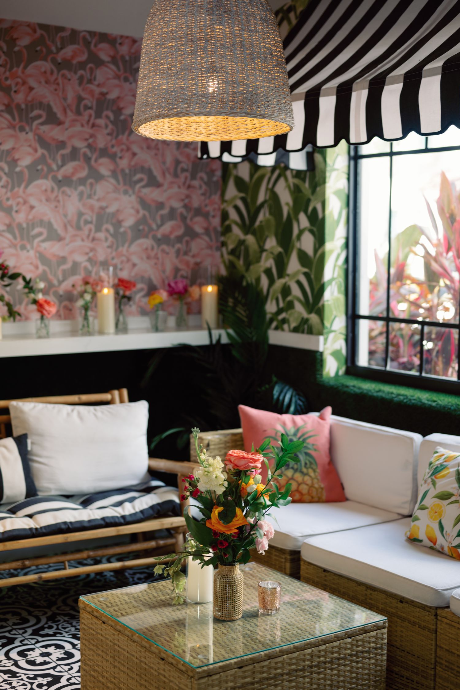 A cozy lounge area with pink floral wallpaper, striped awning, wicker furniture, and a textured pendant light.