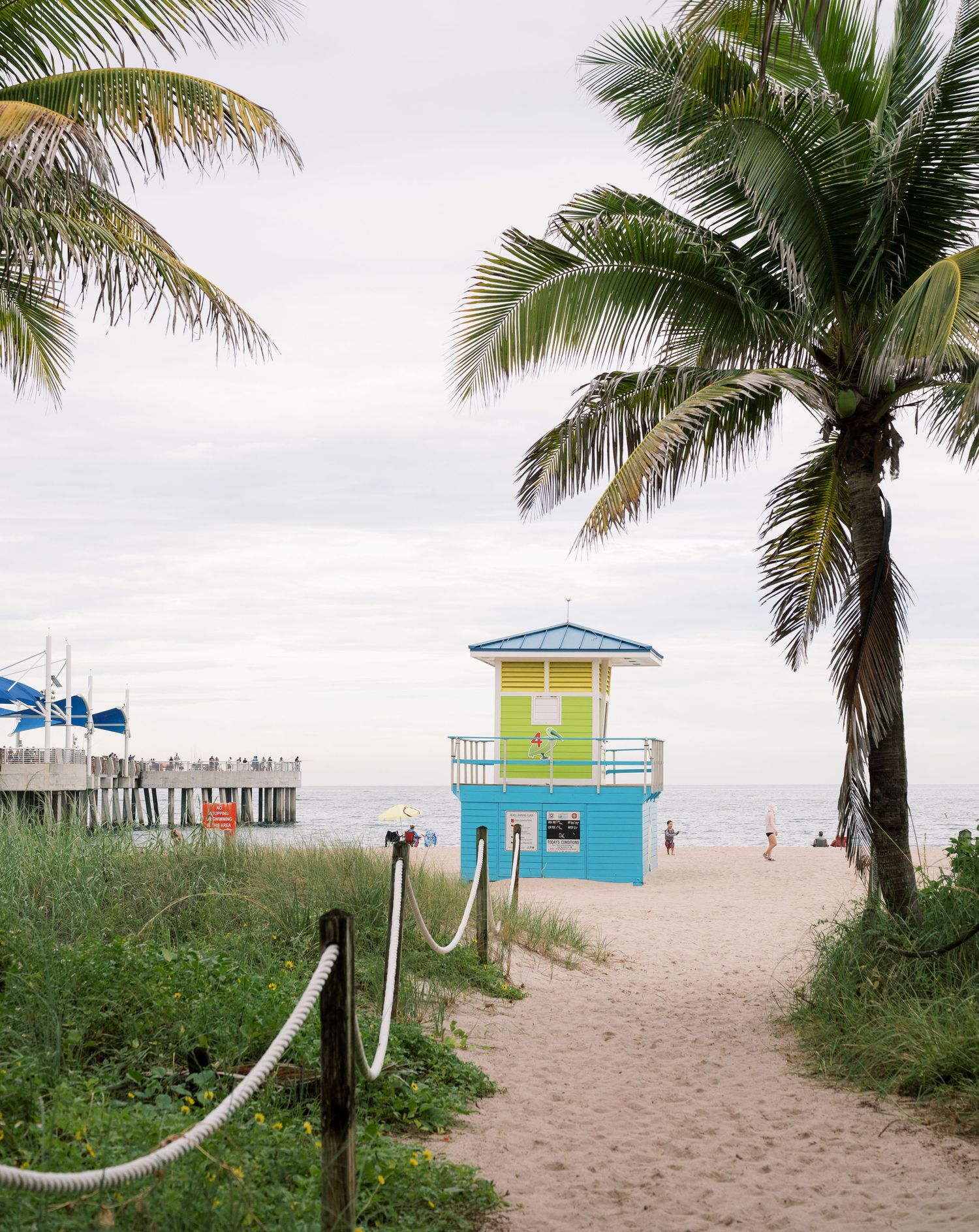 A row of lifeguard stations with colorful pastel paint line the sandy beach under palm trees in Miami Beach.
