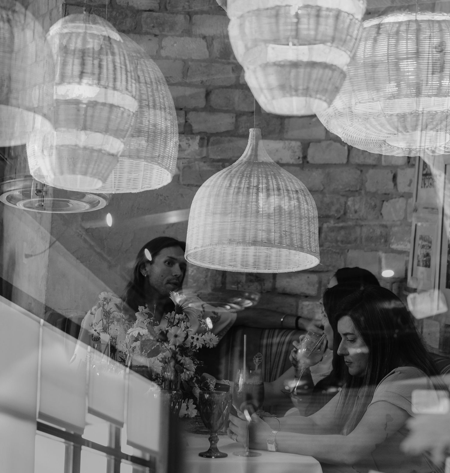 A black and white photo of diners beneath woven pendant lights in a restaurant.