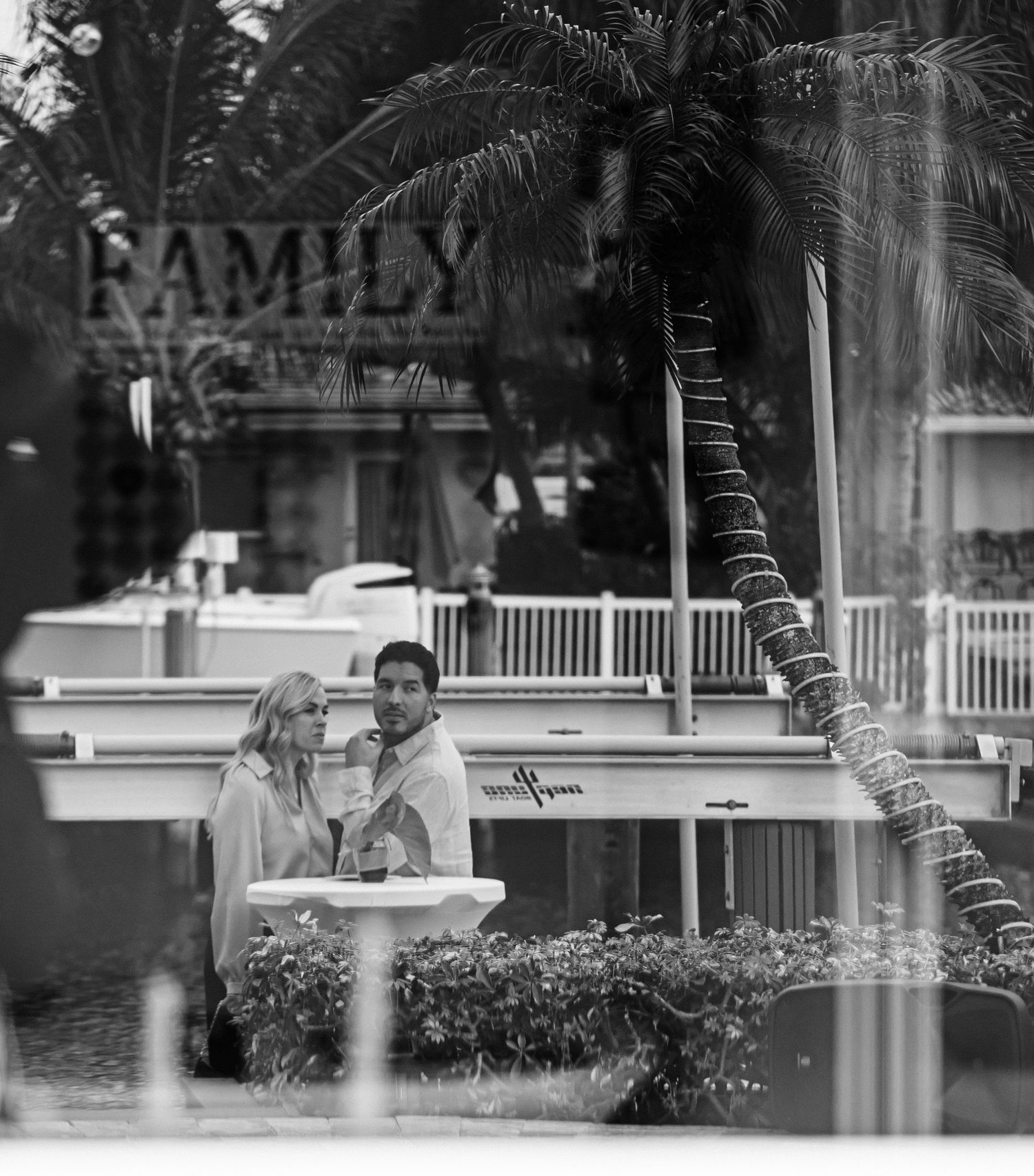 Black and white view of an outdoor patio area with palm trees and furniture.