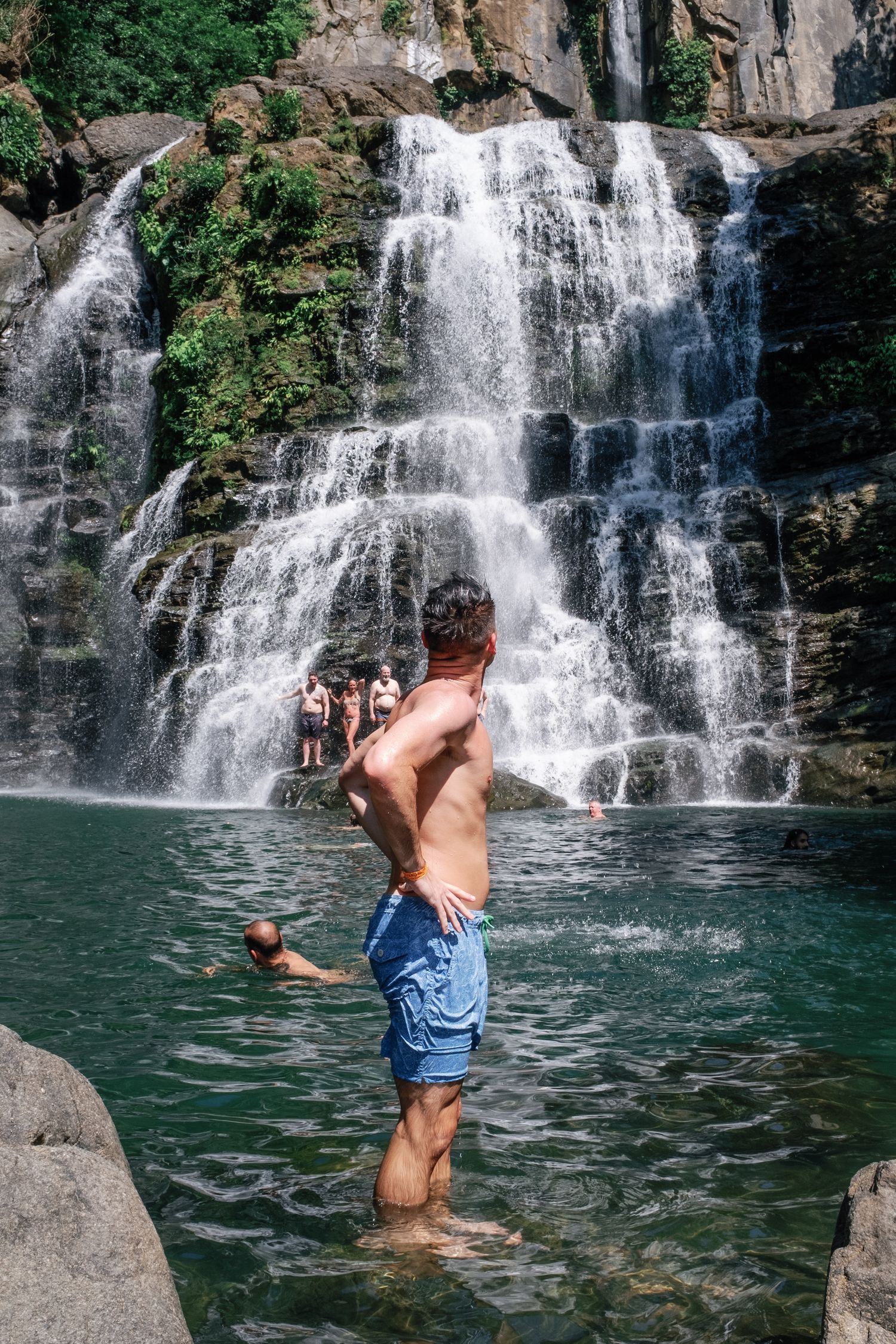 A sequence showing someone jumping into a scenic waterfall pool surrounded by rocks and lush vegetation.