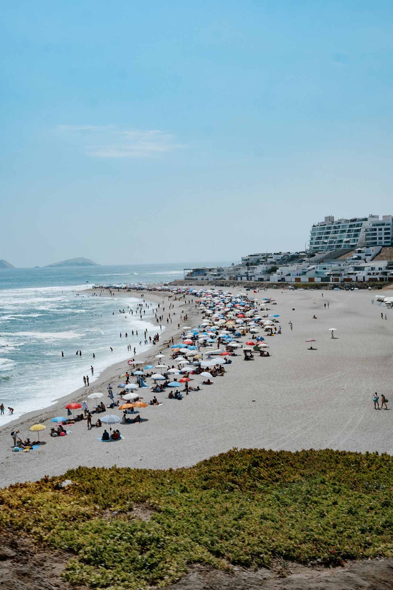 Panoramic view of a sandy beach with colorful umbrellas and beachgoers dotting the shoreline along the ocean coast.