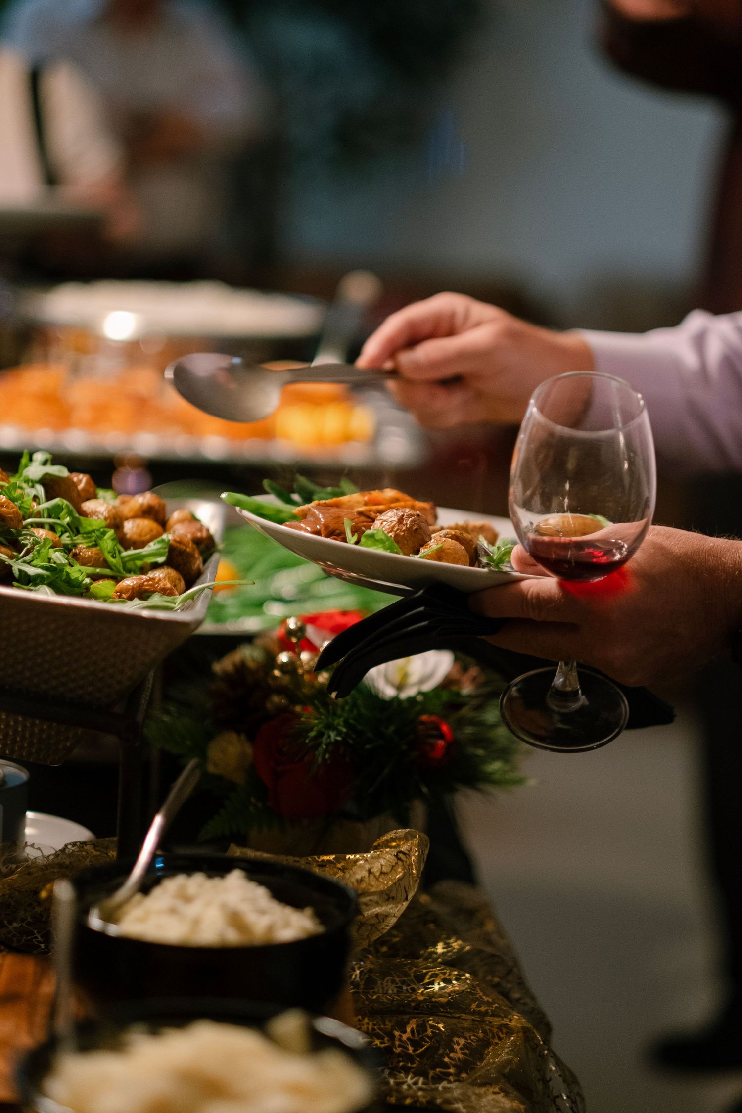 Hands holding plates of colorful food and wine glasses at an elegant dinner gathering.