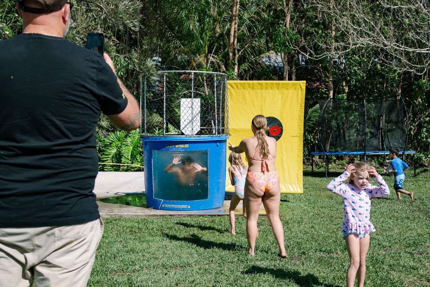 A group of people enjoying outdoor activities on a sunny day in a grassy park area with playground equipment.